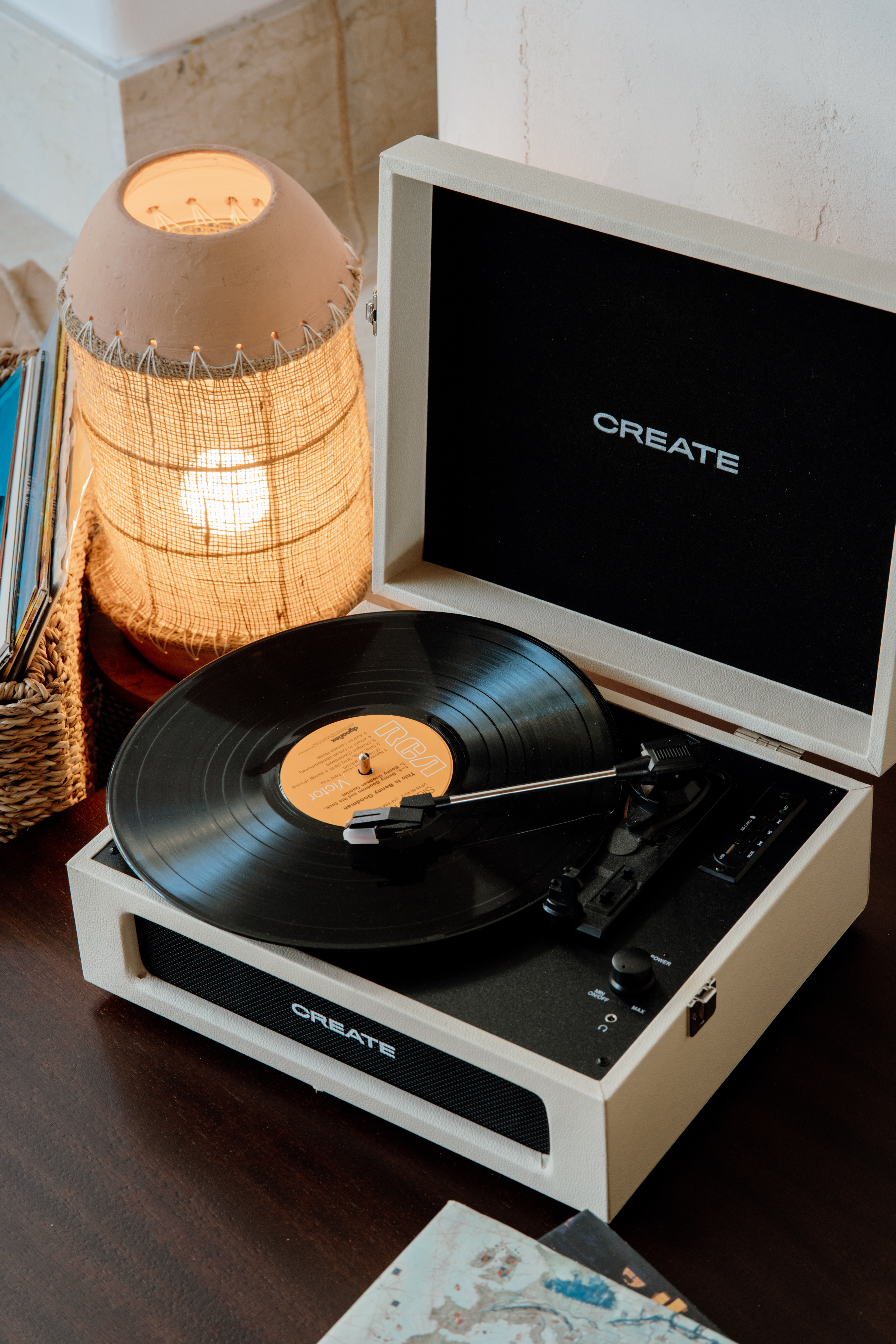 Vintage cream CREATE record player playing vinyl, beside warm burlap lamp.
