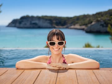 Smiling woman in sunglasses, infinity pool with ocean and coastal view.