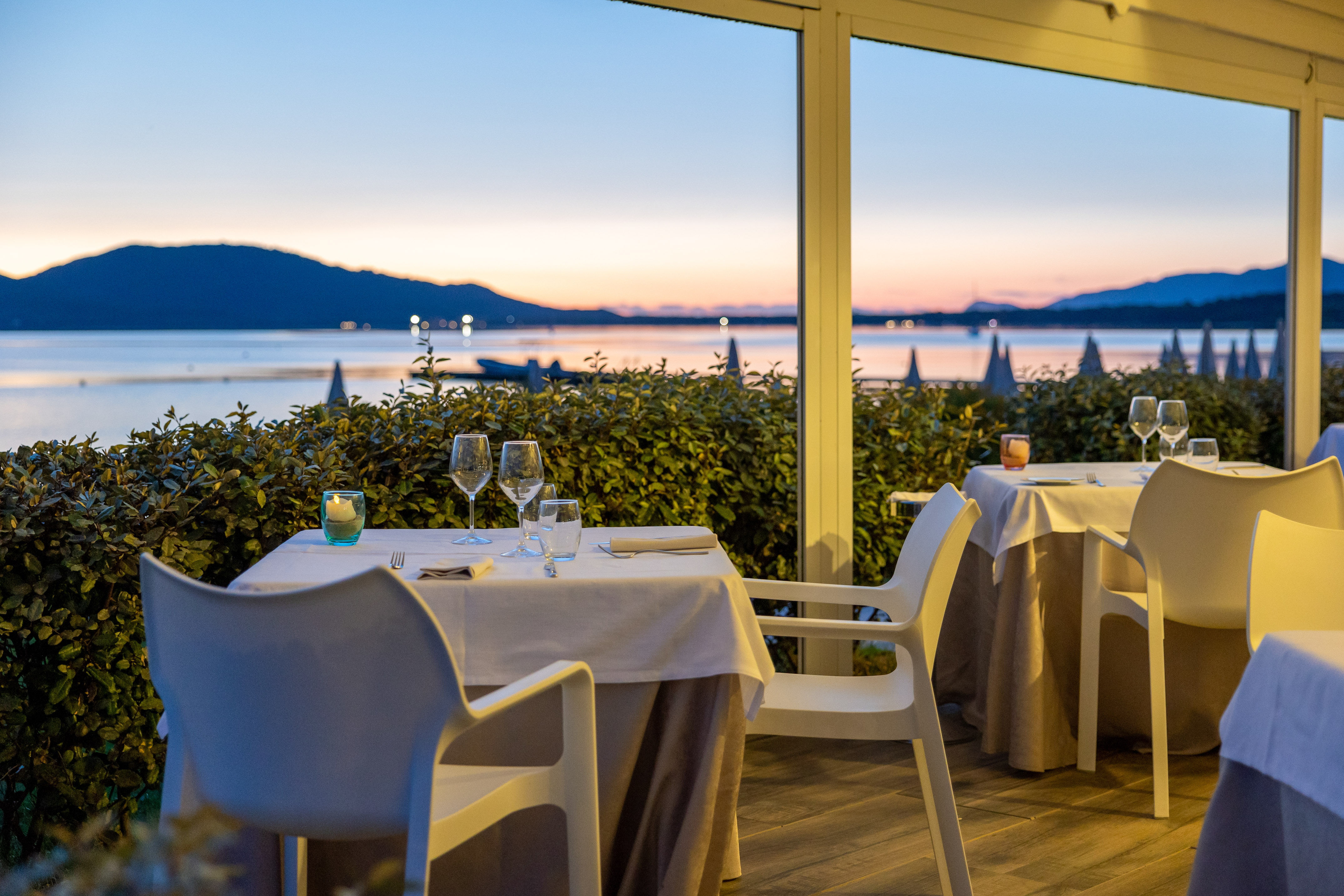 Outdoor restaurant tables with lake and mountain view at sunset.