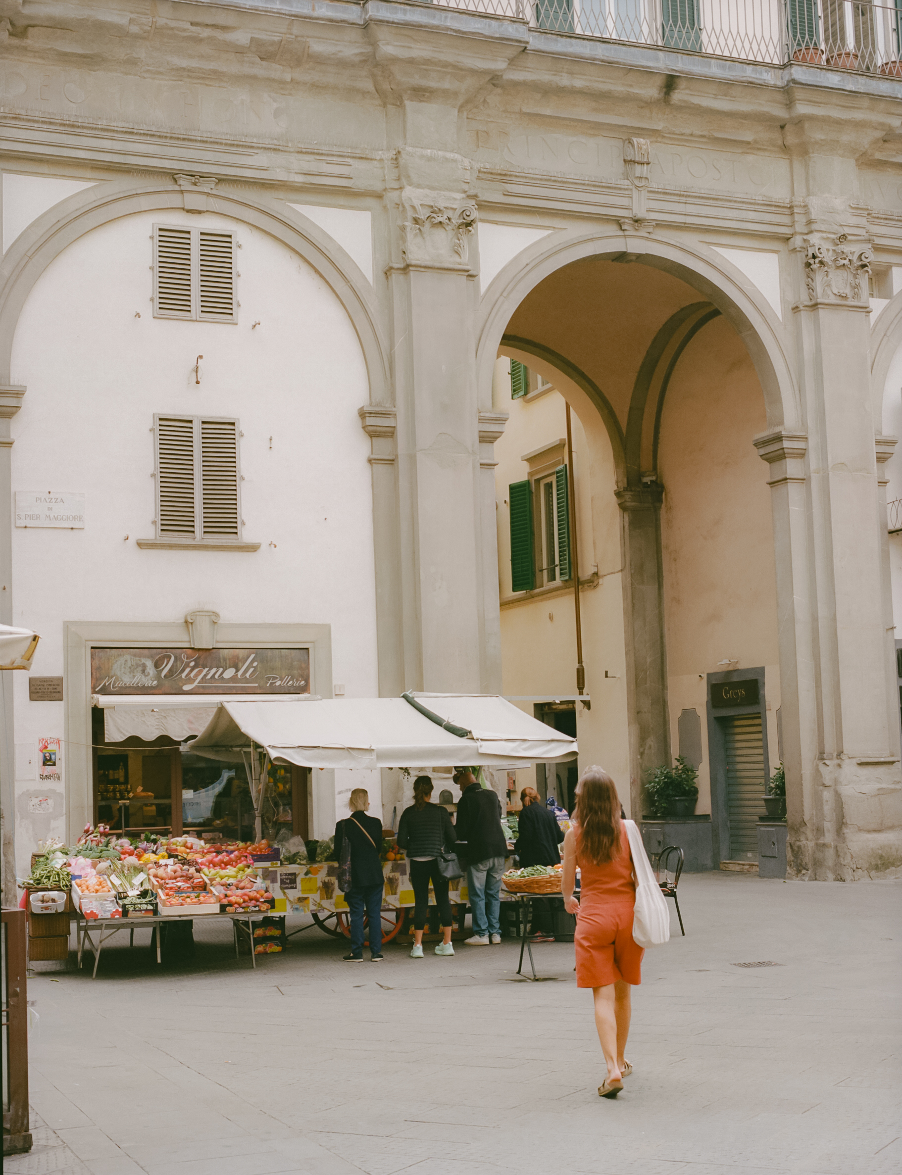 a woman walking in front of a fruit stand