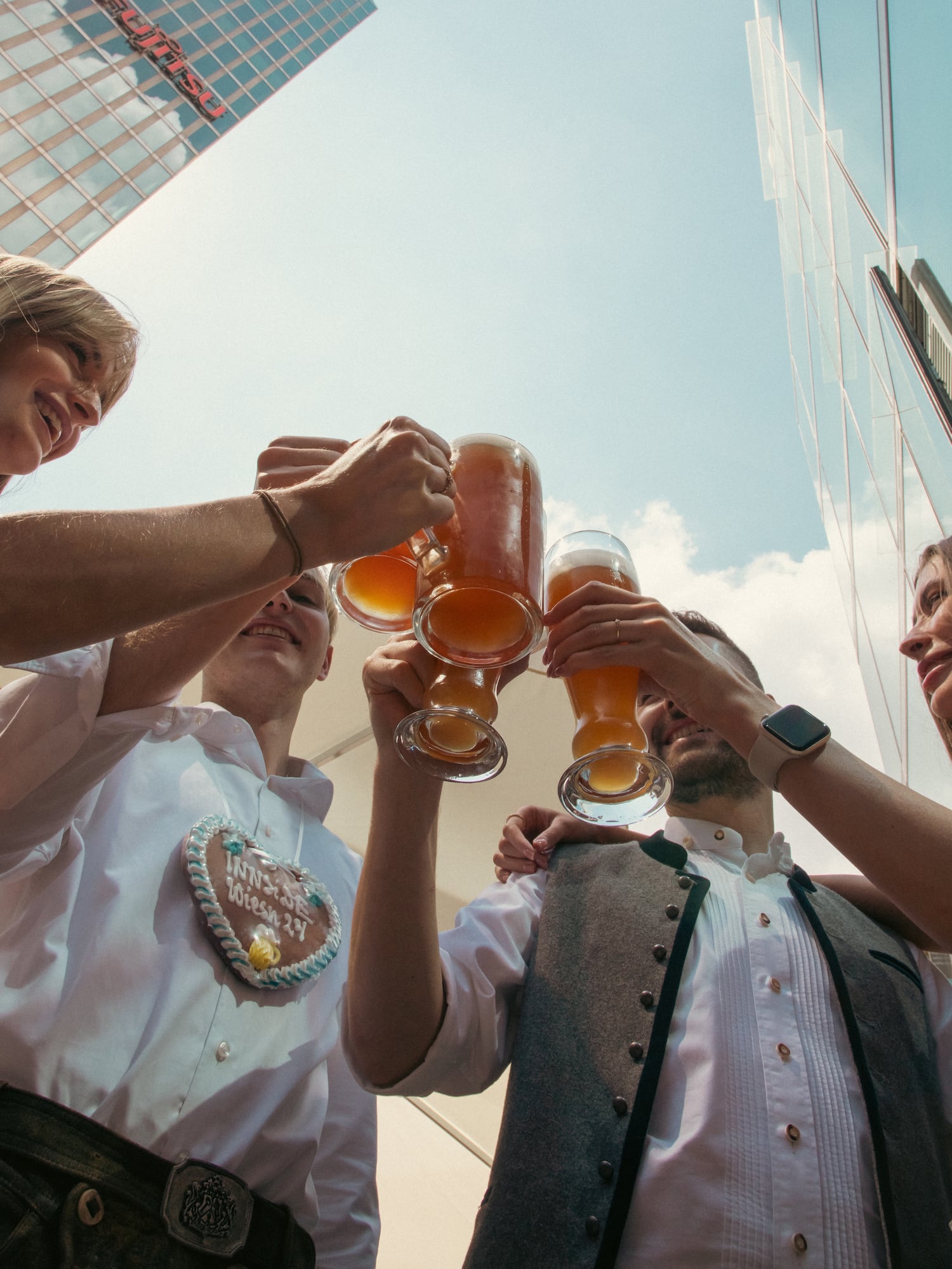 Friends in traditional attire toast beer steins at urban Oktoberfest.