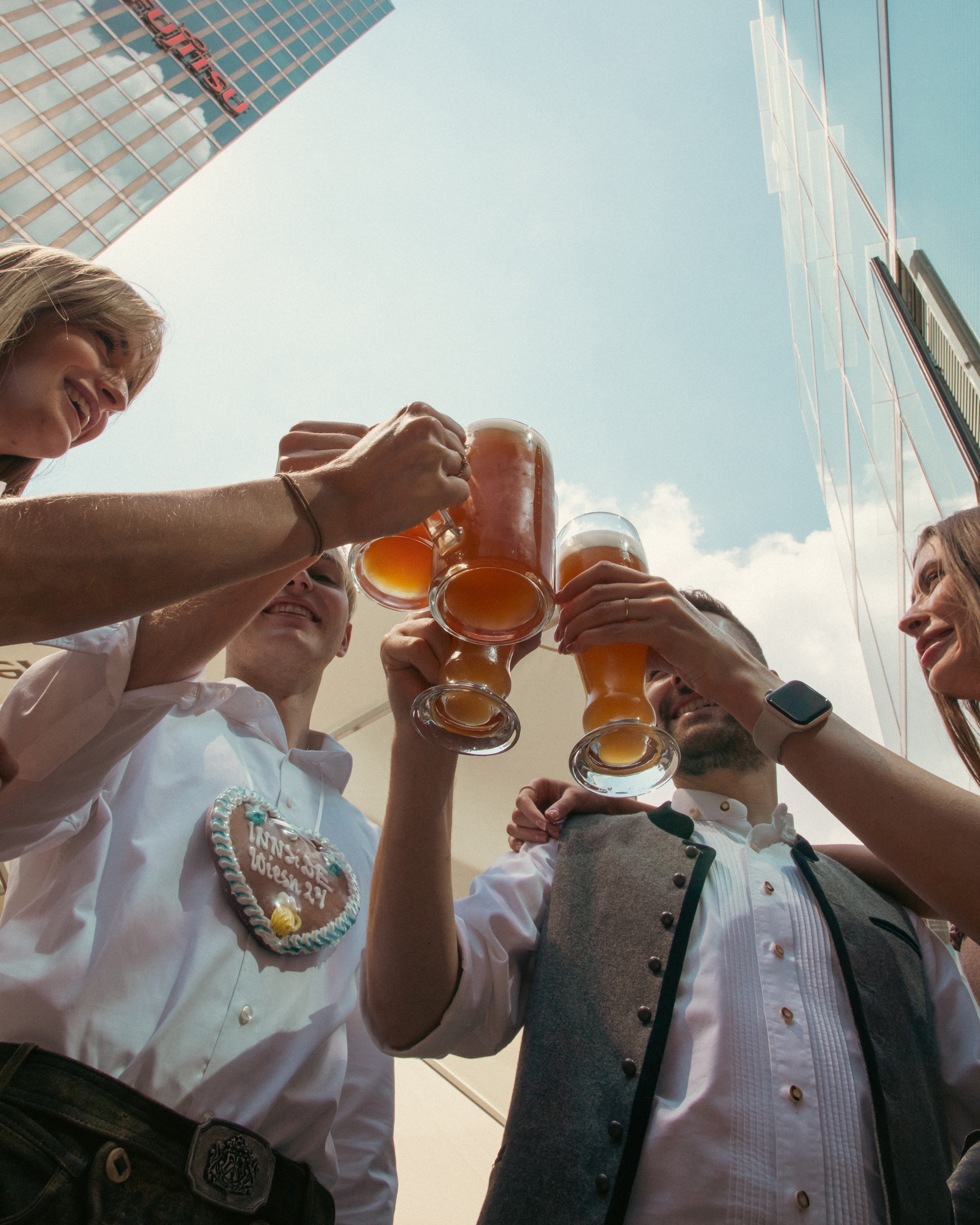 Friends in traditional attire toast beer steins at urban Oktoberfest.