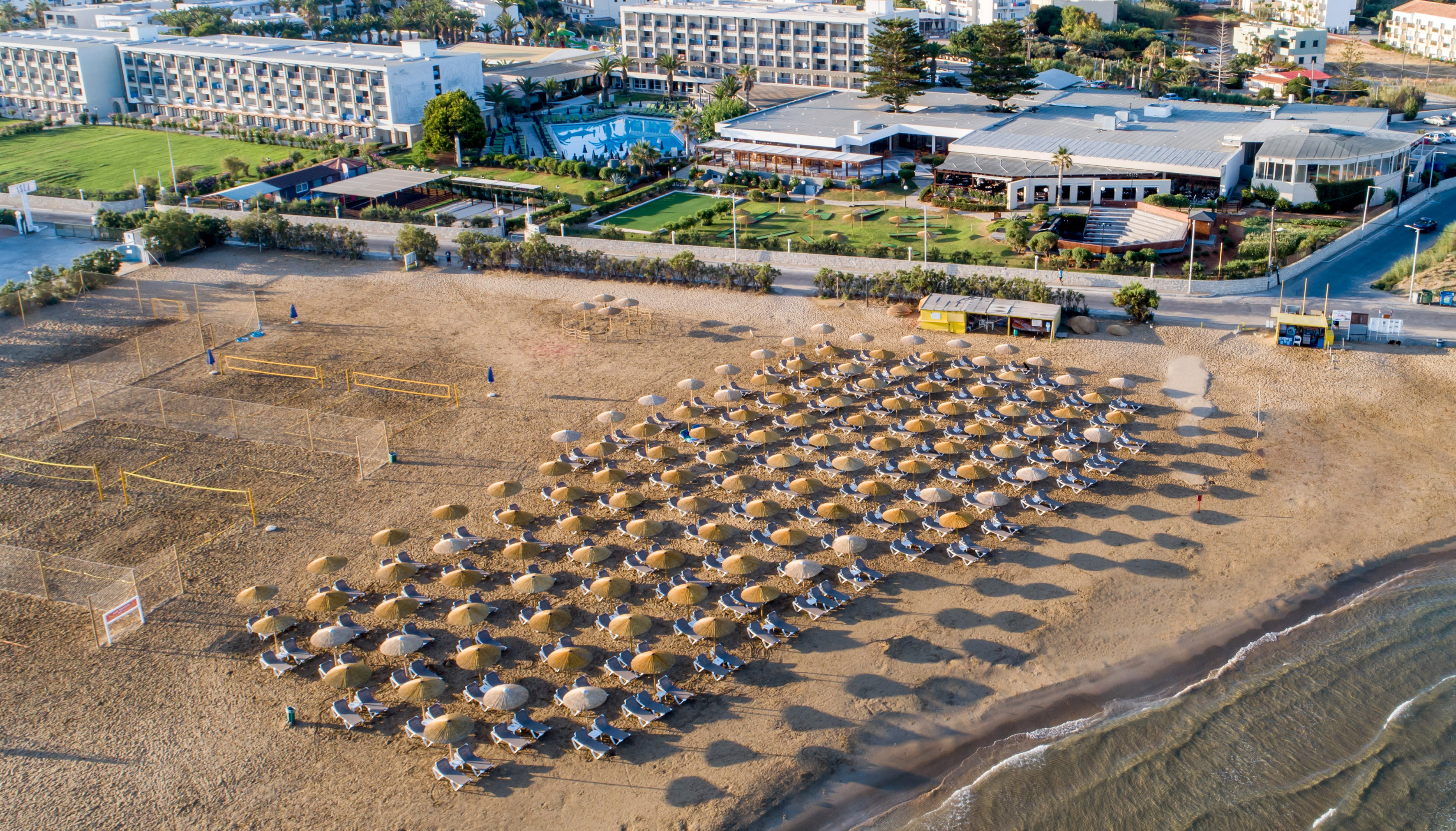 Sunny resort beach aerial with umbrellas, sun loungers, hotel, and ocean.