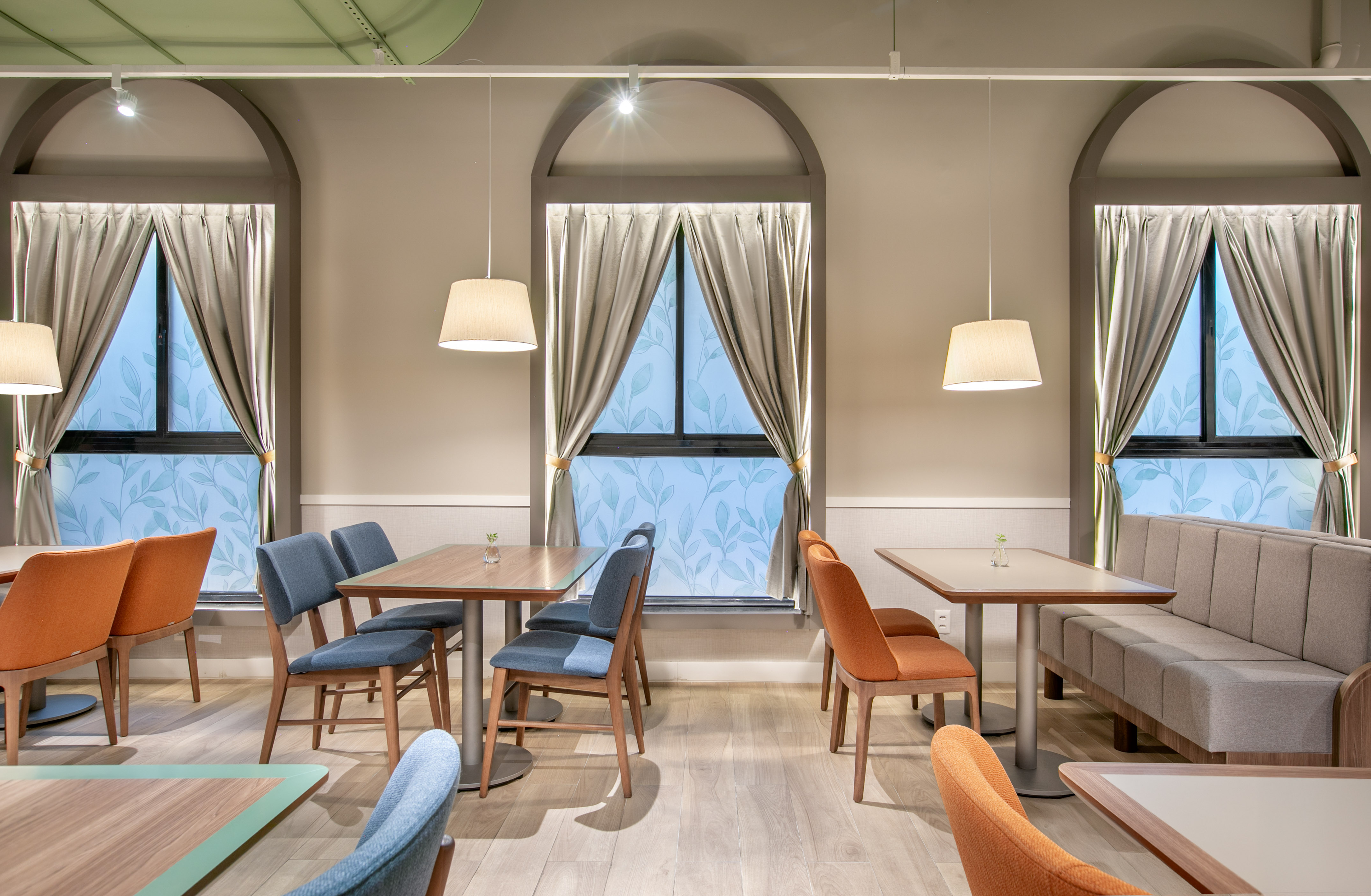 Cafe dining room with arched windows, wooden tables, and upholstered chairs.