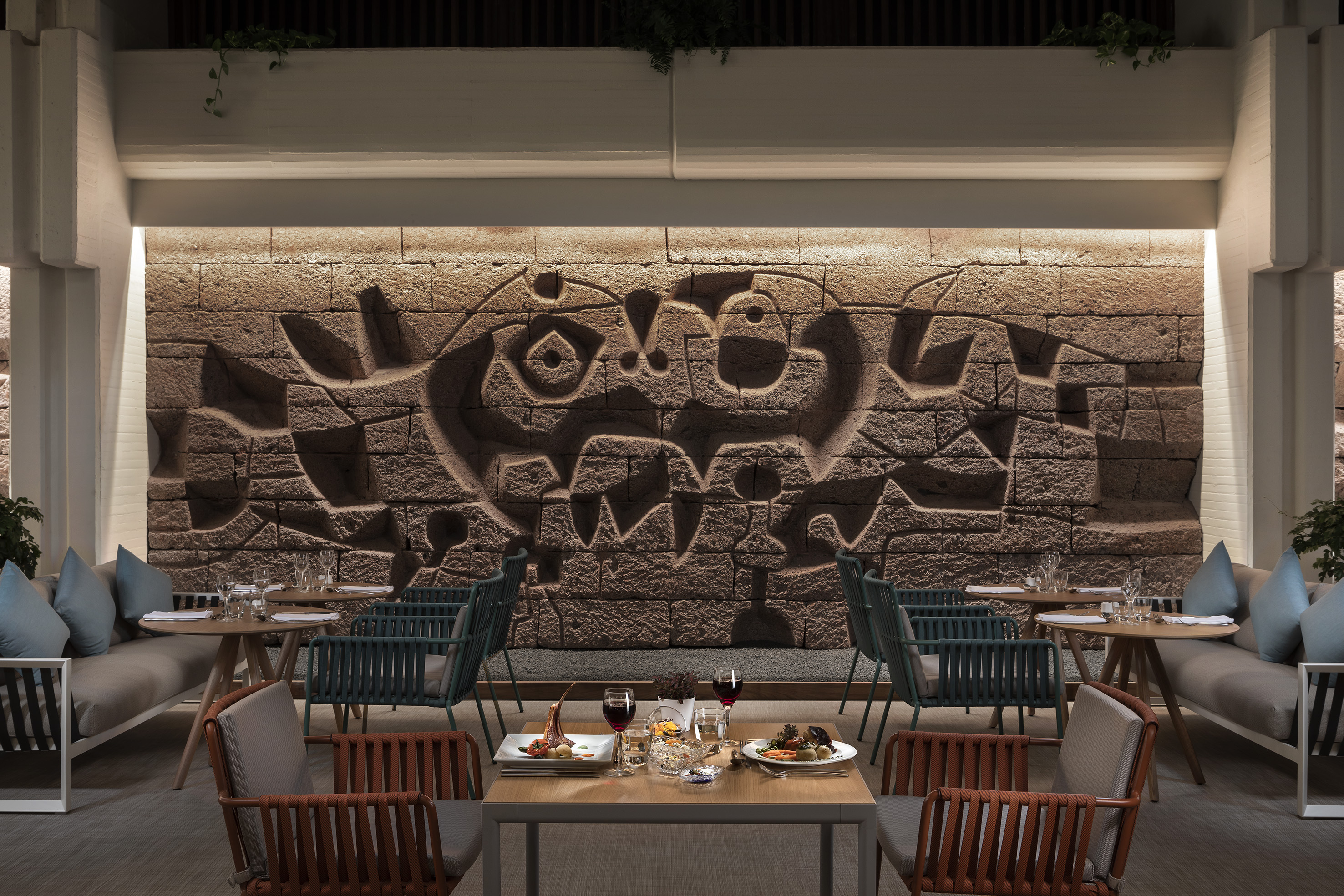 Modern restaurant with artistic carved stone wall and elegant dining setup.