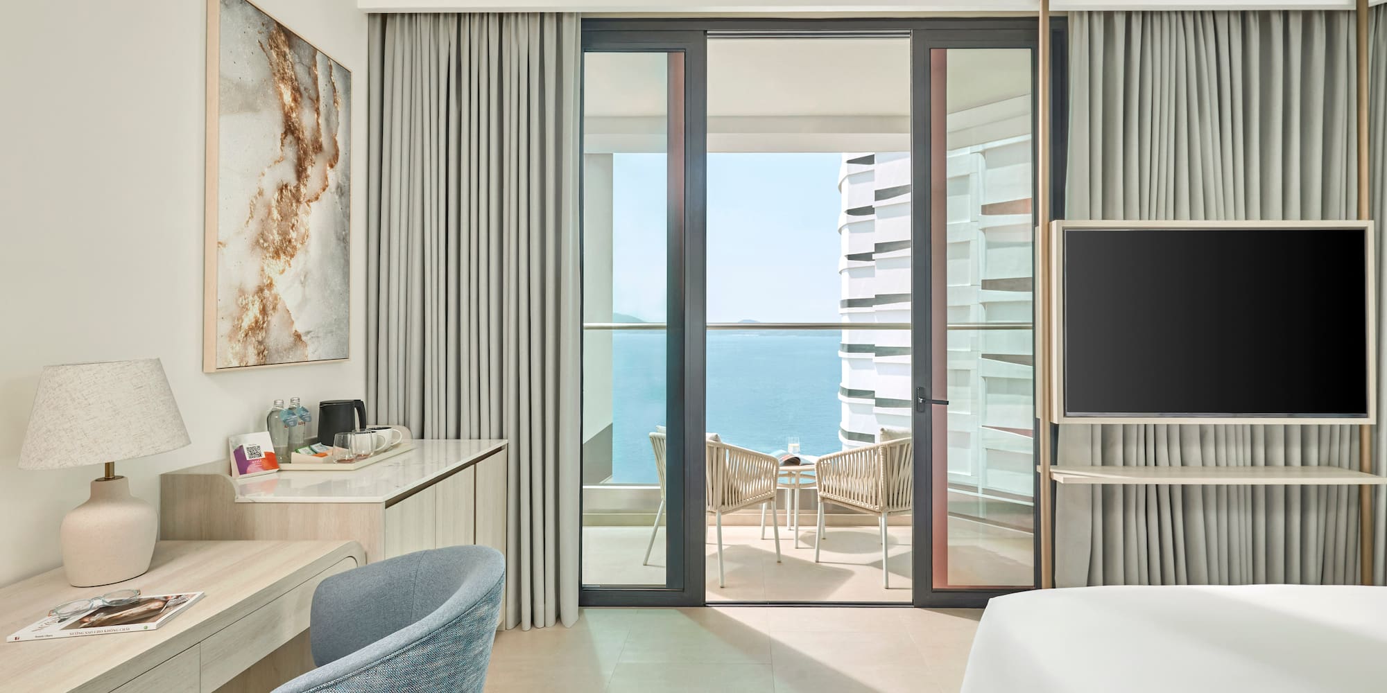 Modern hotel room with ocean view balcony, desk, and sleek design.