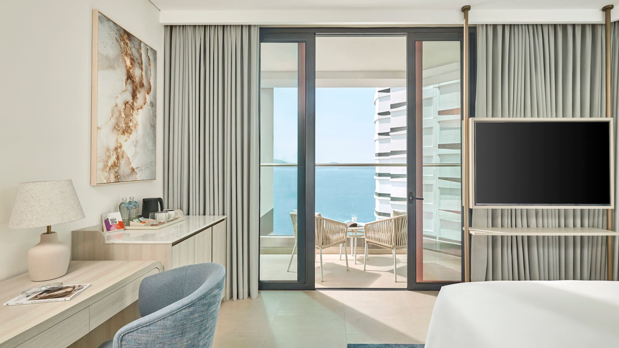 Modern hotel room with ocean view balcony, desk, and sleek design.