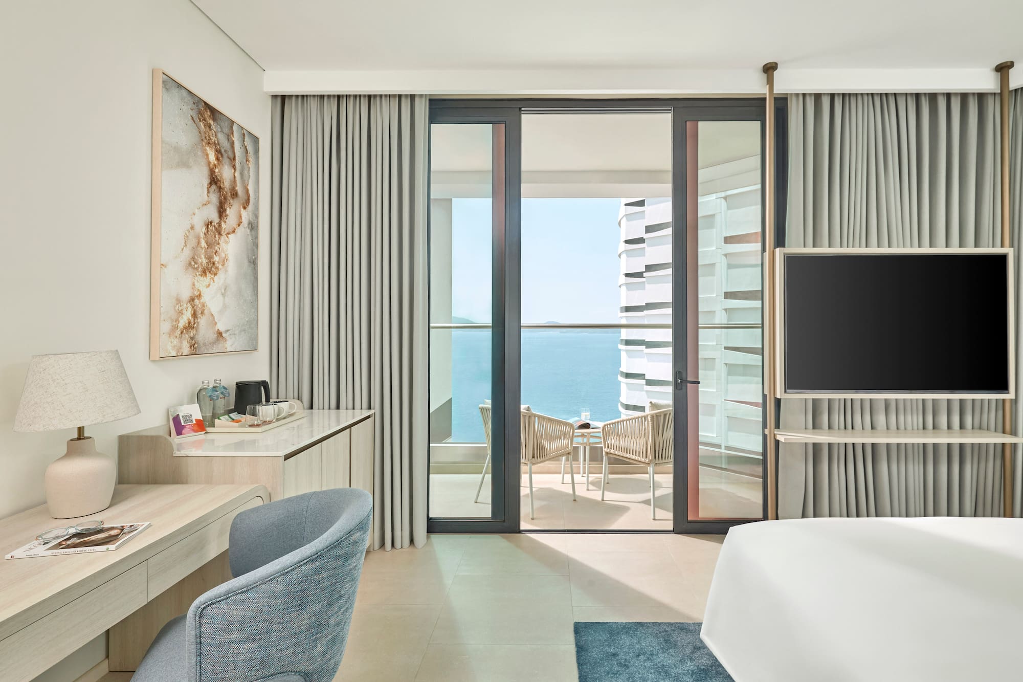 Modern hotel room with ocean view balcony, desk, and sleek design.