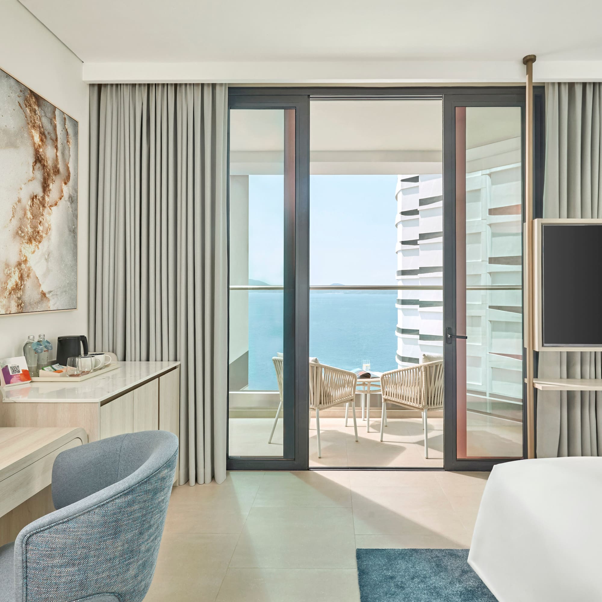 Modern hotel room with ocean view balcony, desk, and sleek design.