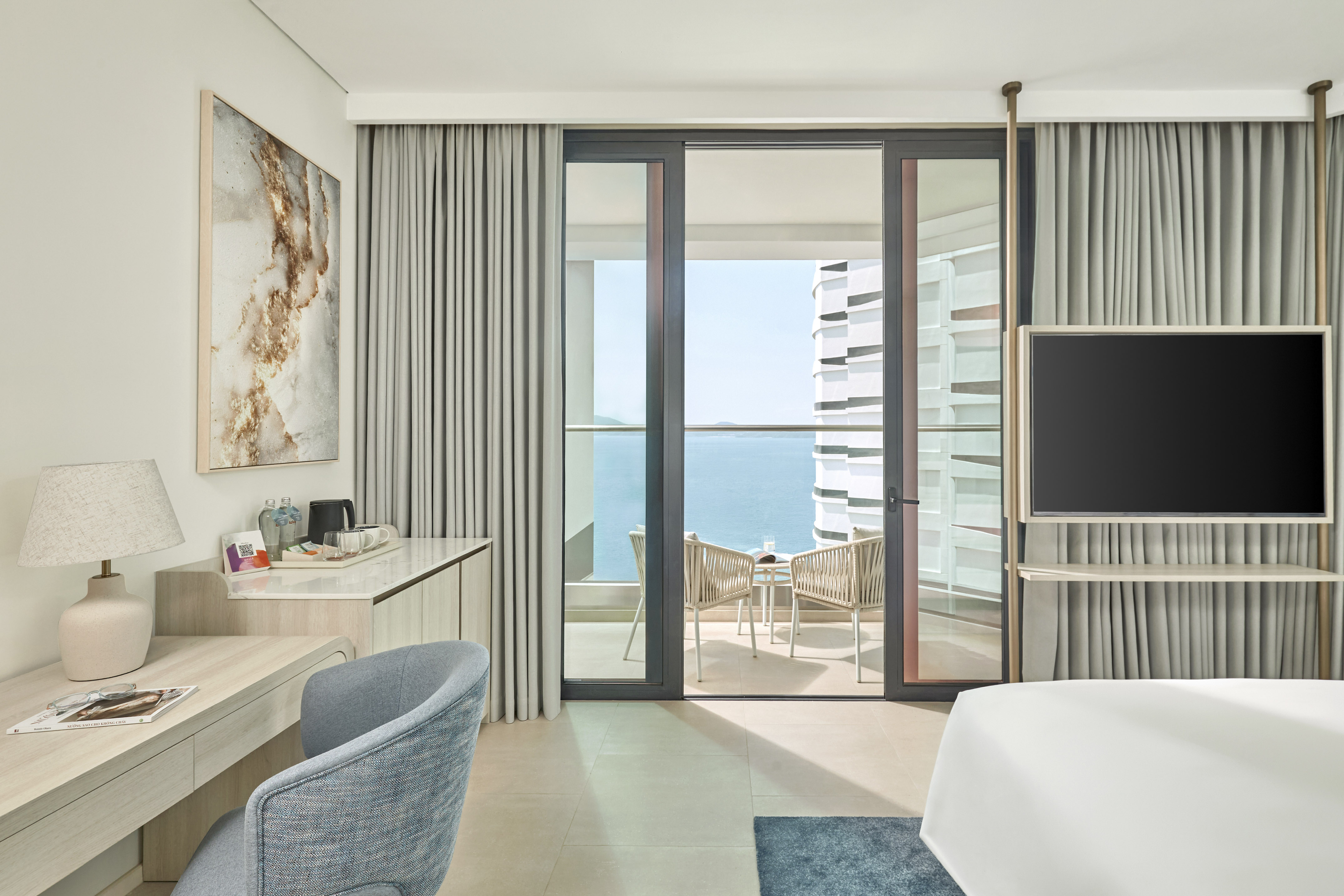 Modern hotel room with ocean view balcony, desk, and sleek design.