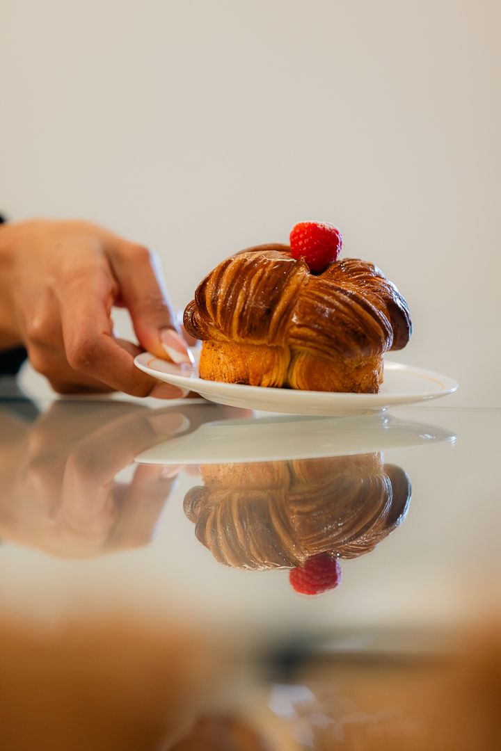 Hand placing glossy, golden pastry with raspberry on white plate.
