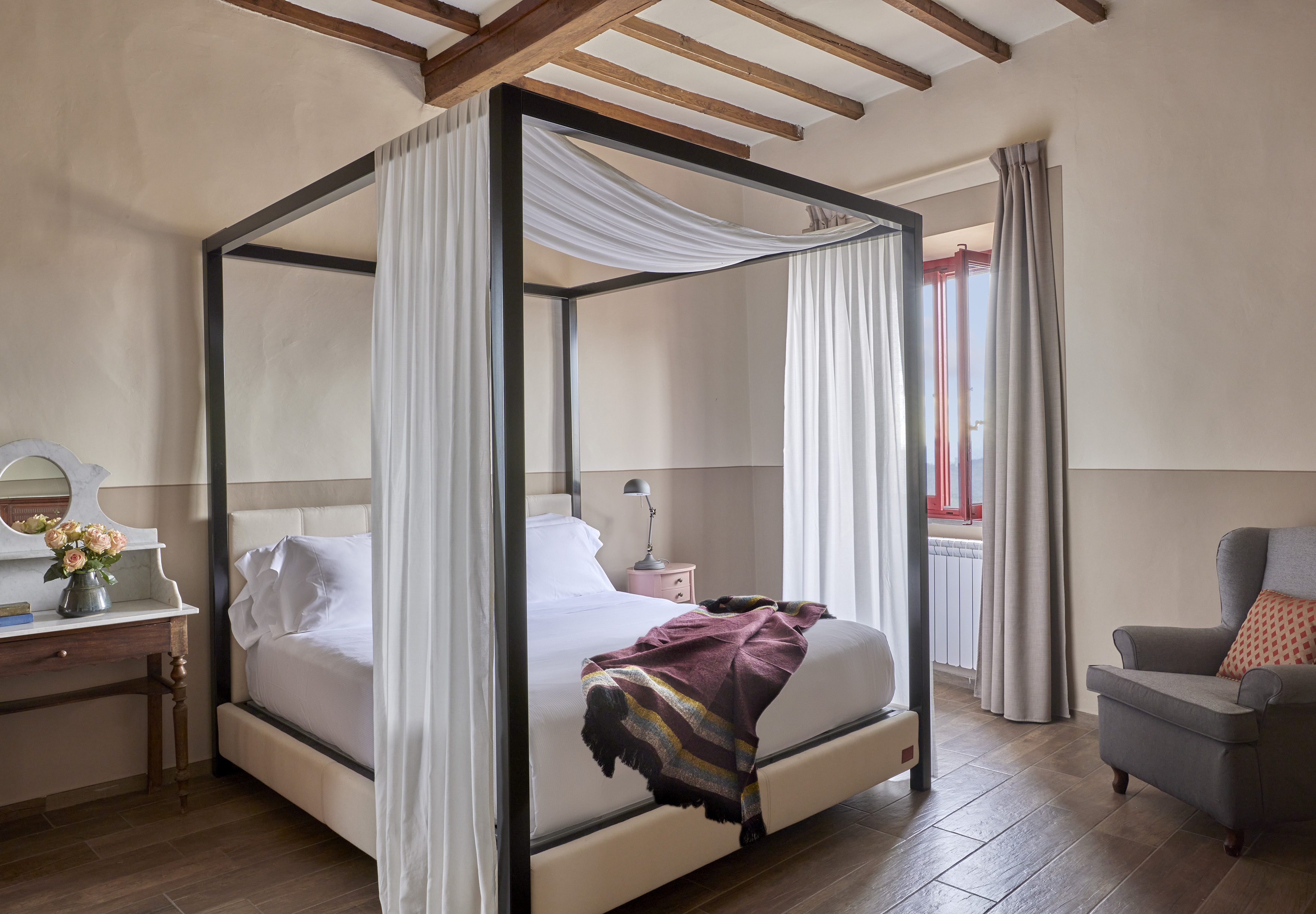 Elegant bedroom with four-poster bed, exposed wooden beams, and armchair.