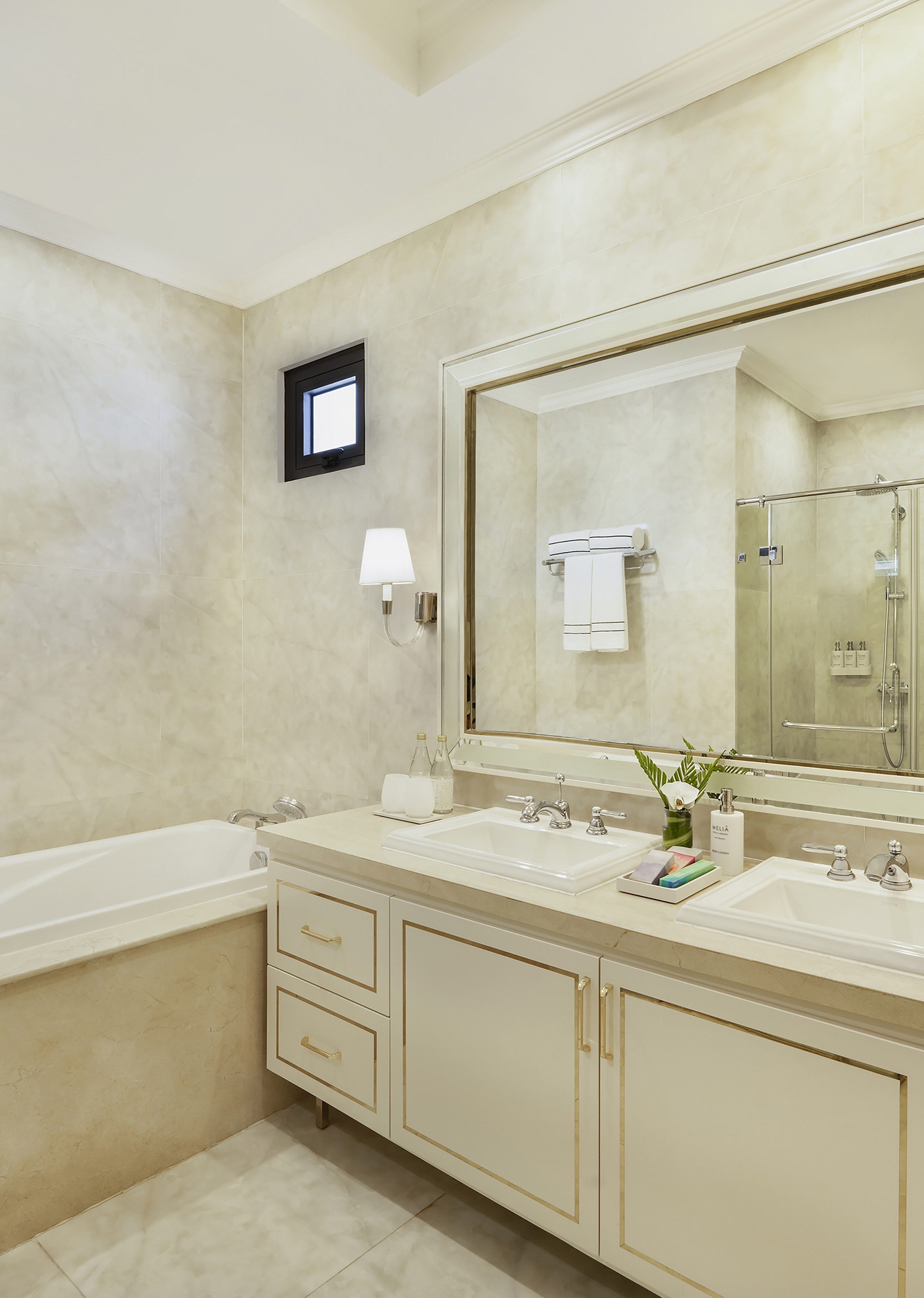 Luxury bathroom: double vanity, bathtub, marble walls, gold trim.