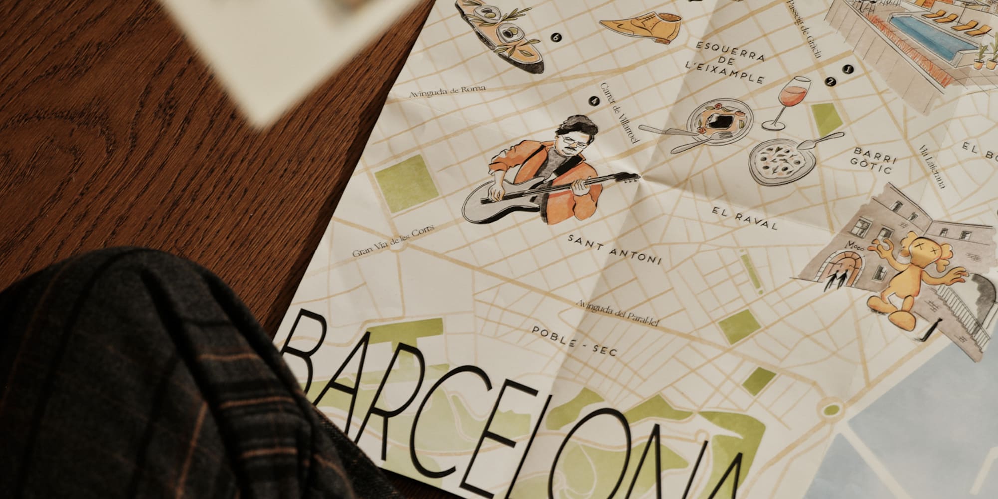 Illustrated Barcelona tourist map with travel postcards on a wood floor.
