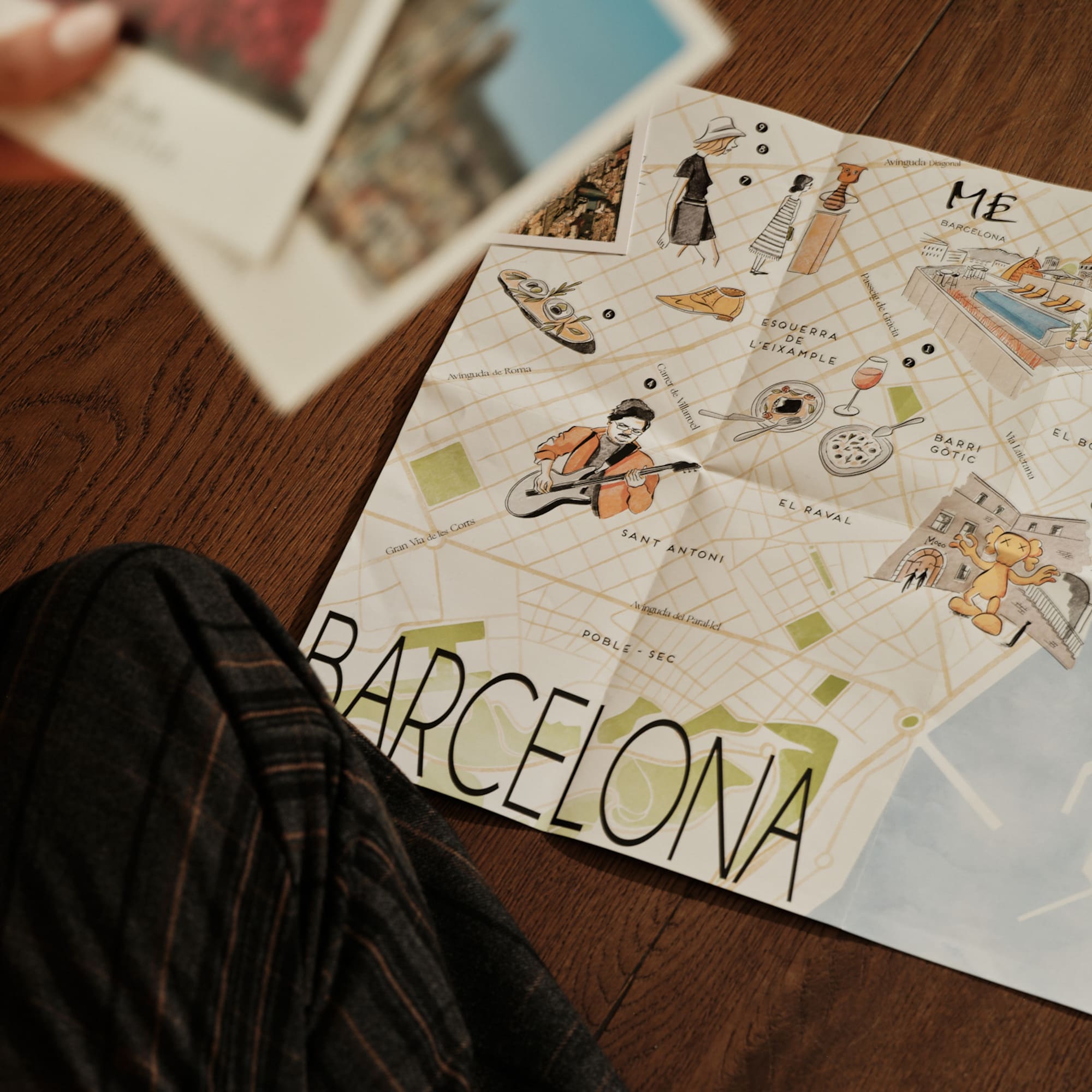 Illustrated Barcelona tourist map with travel postcards on a wood floor.
