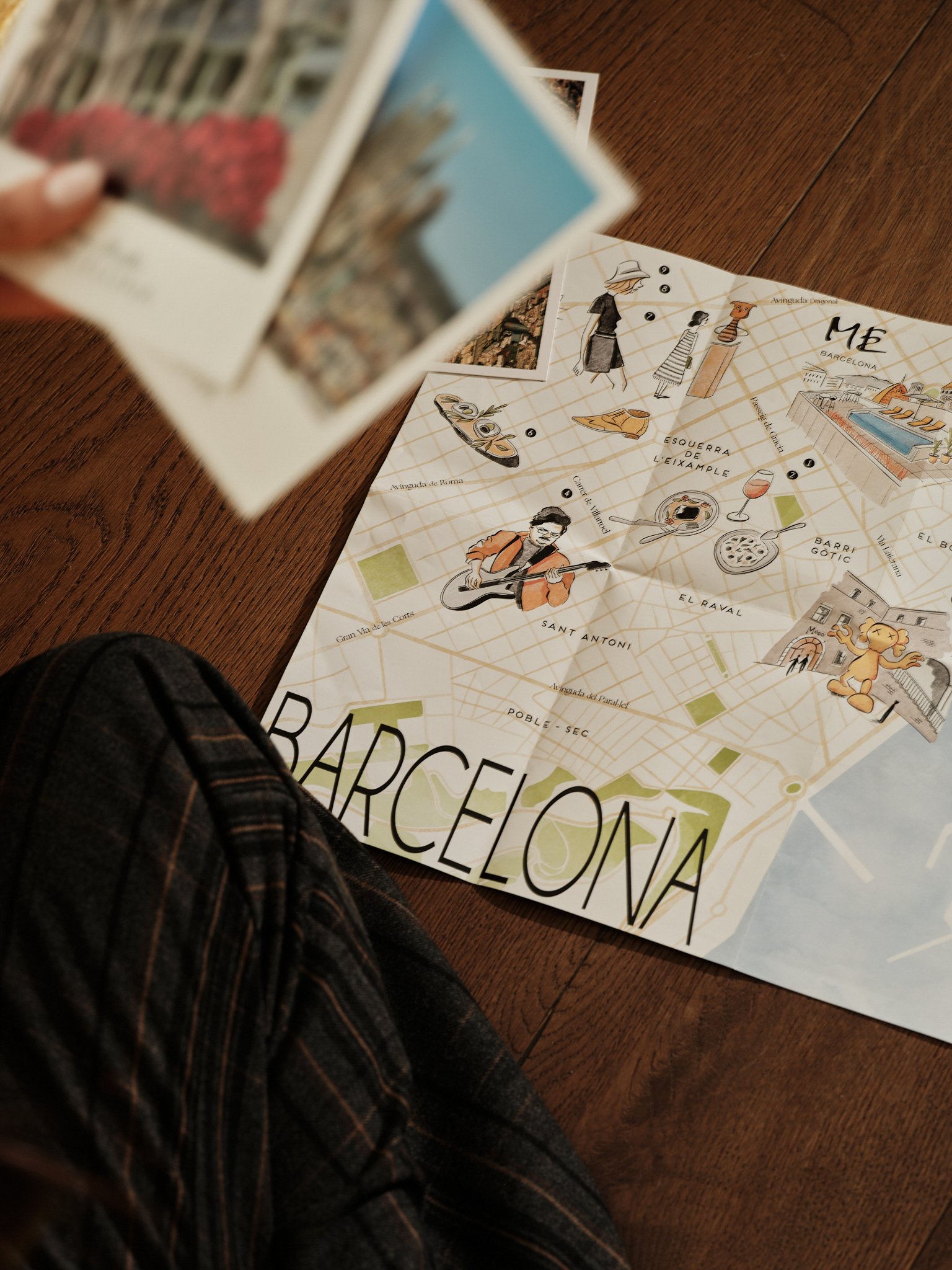 Illustrated Barcelona tourist map with travel postcards on a wood floor.