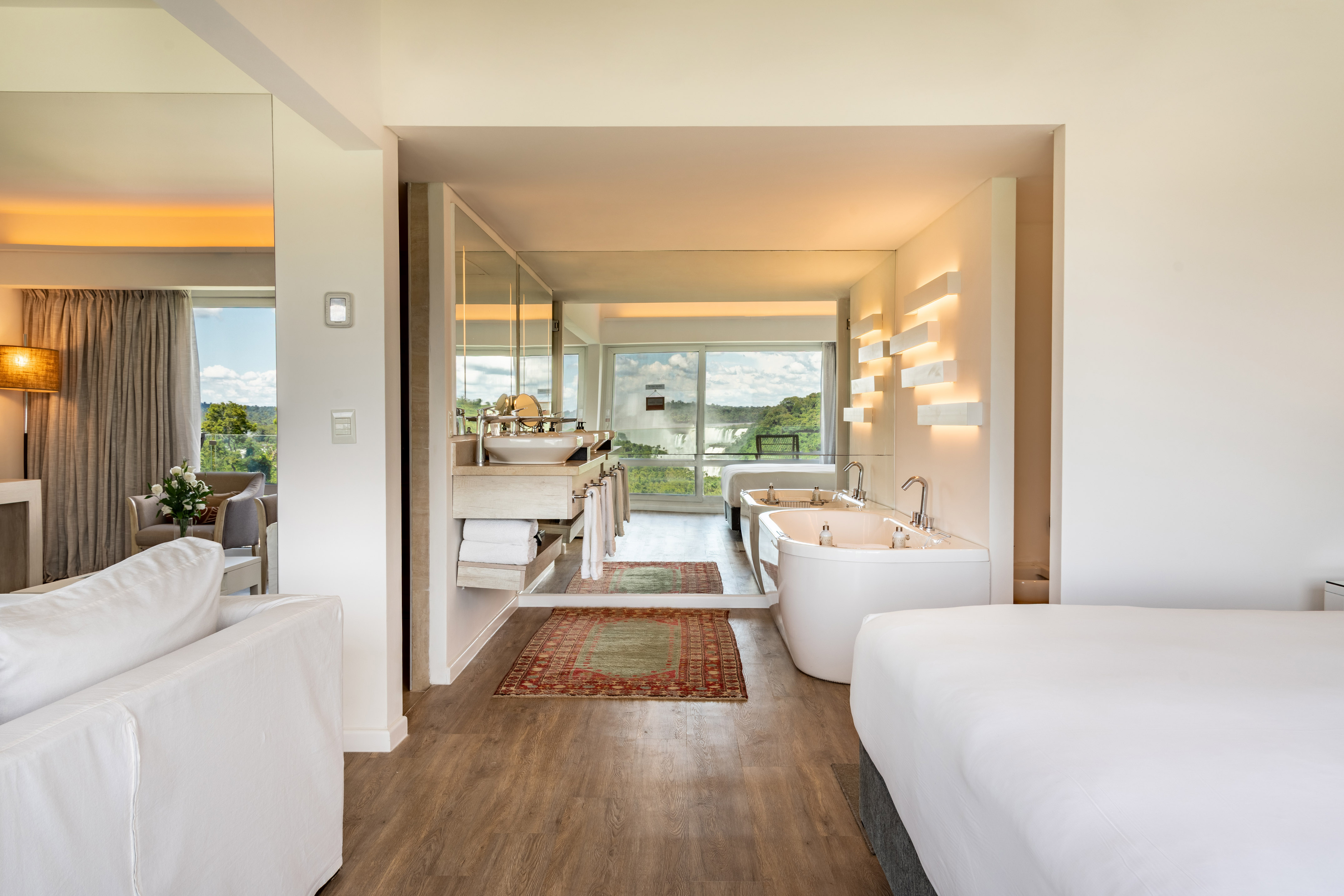 Luxury hotel suite with waterfall view, two soaking tubs, and modern decor.