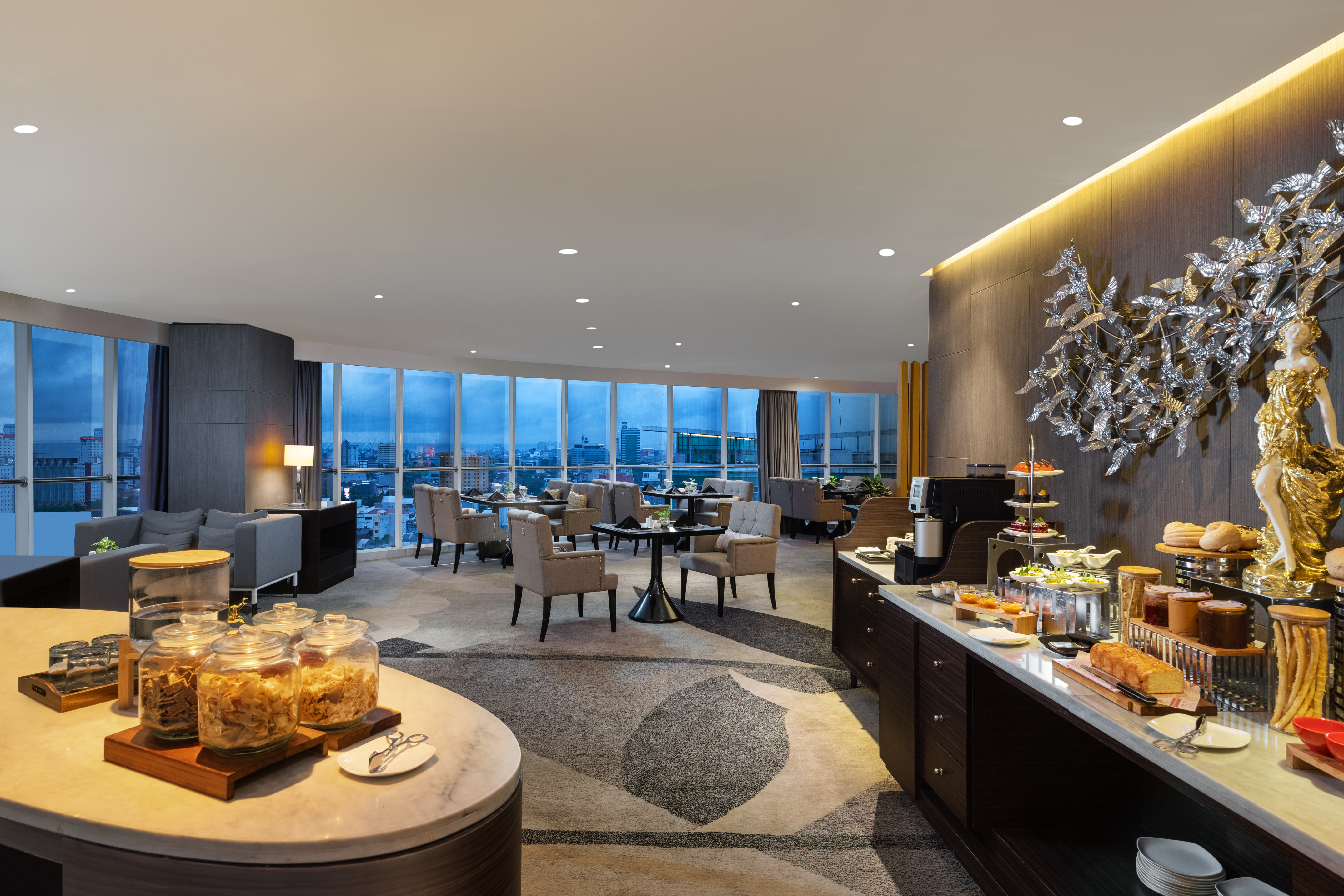 Modern hotel lounge with breakfast buffet, city view, and elegant decor.