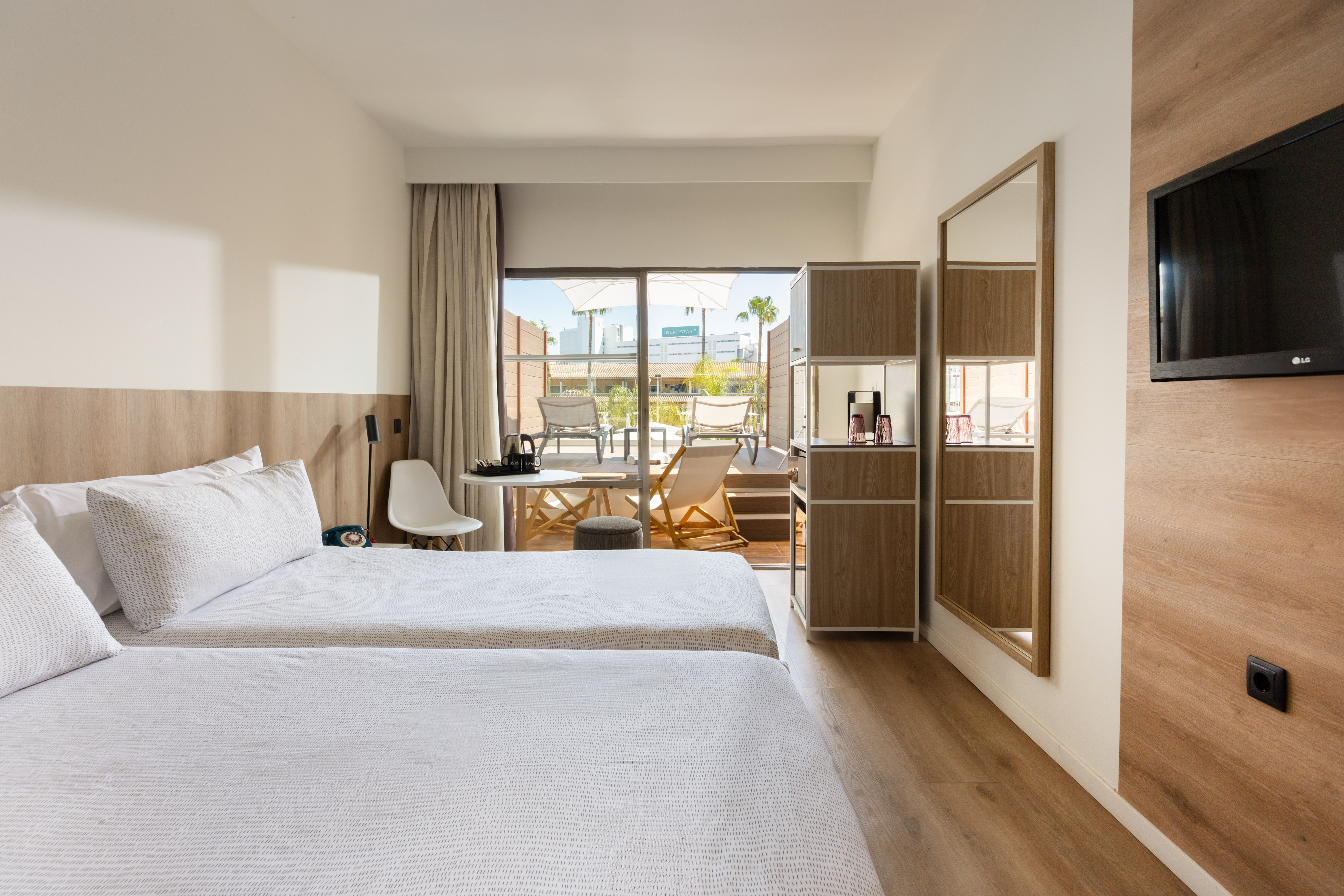 Bright hotel room with twin beds, wooden floors, and a private balcony.