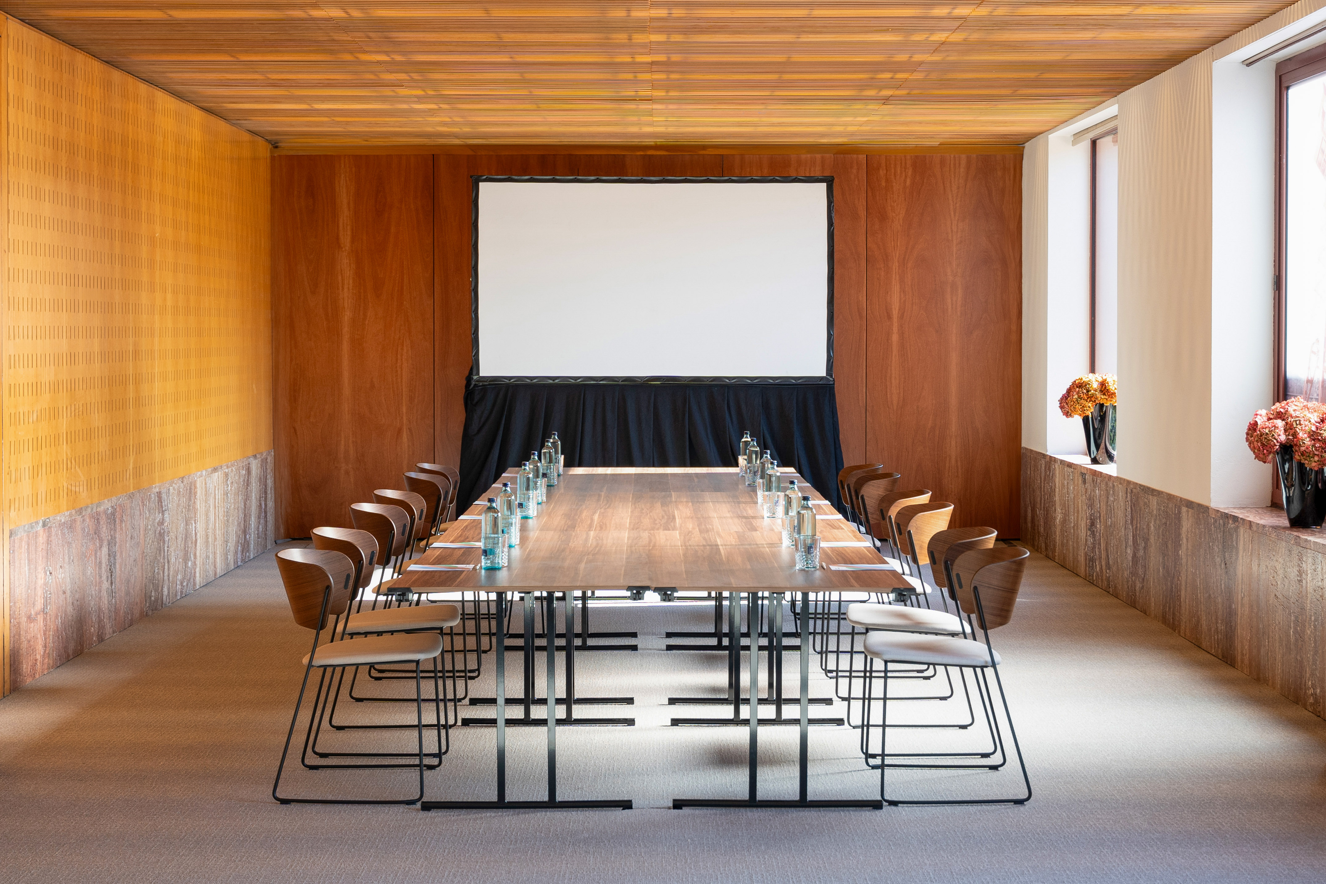 Modern conference room with large wooden table, chairs, and projection screen.