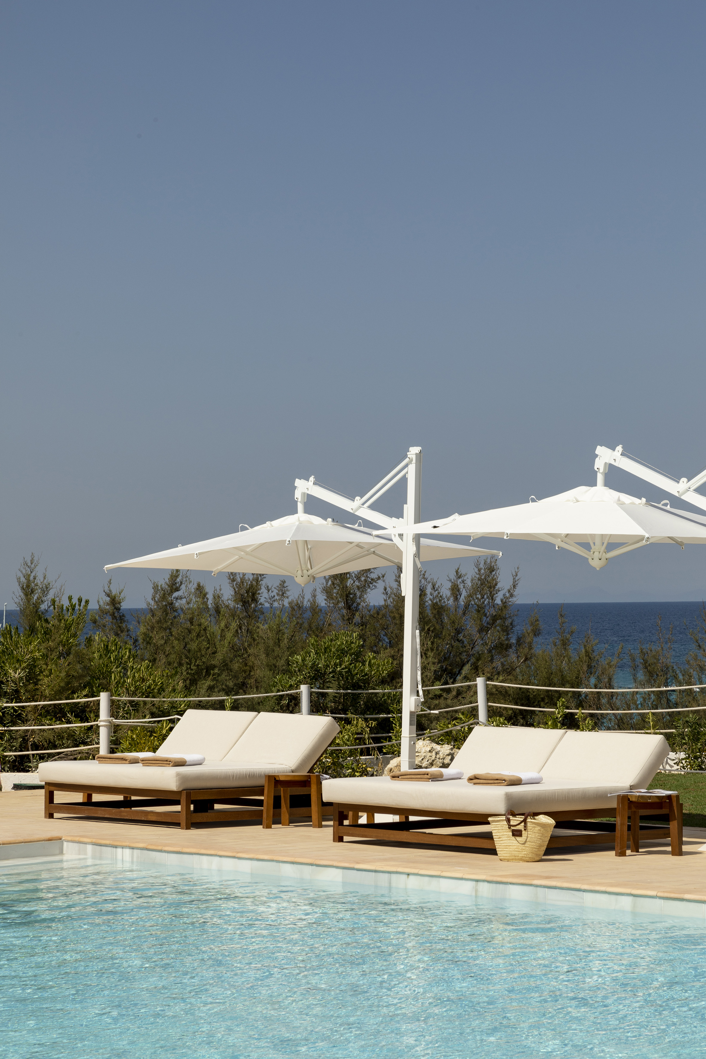 Luxury poolside with lounge chairs, white umbrellas, and ocean view.