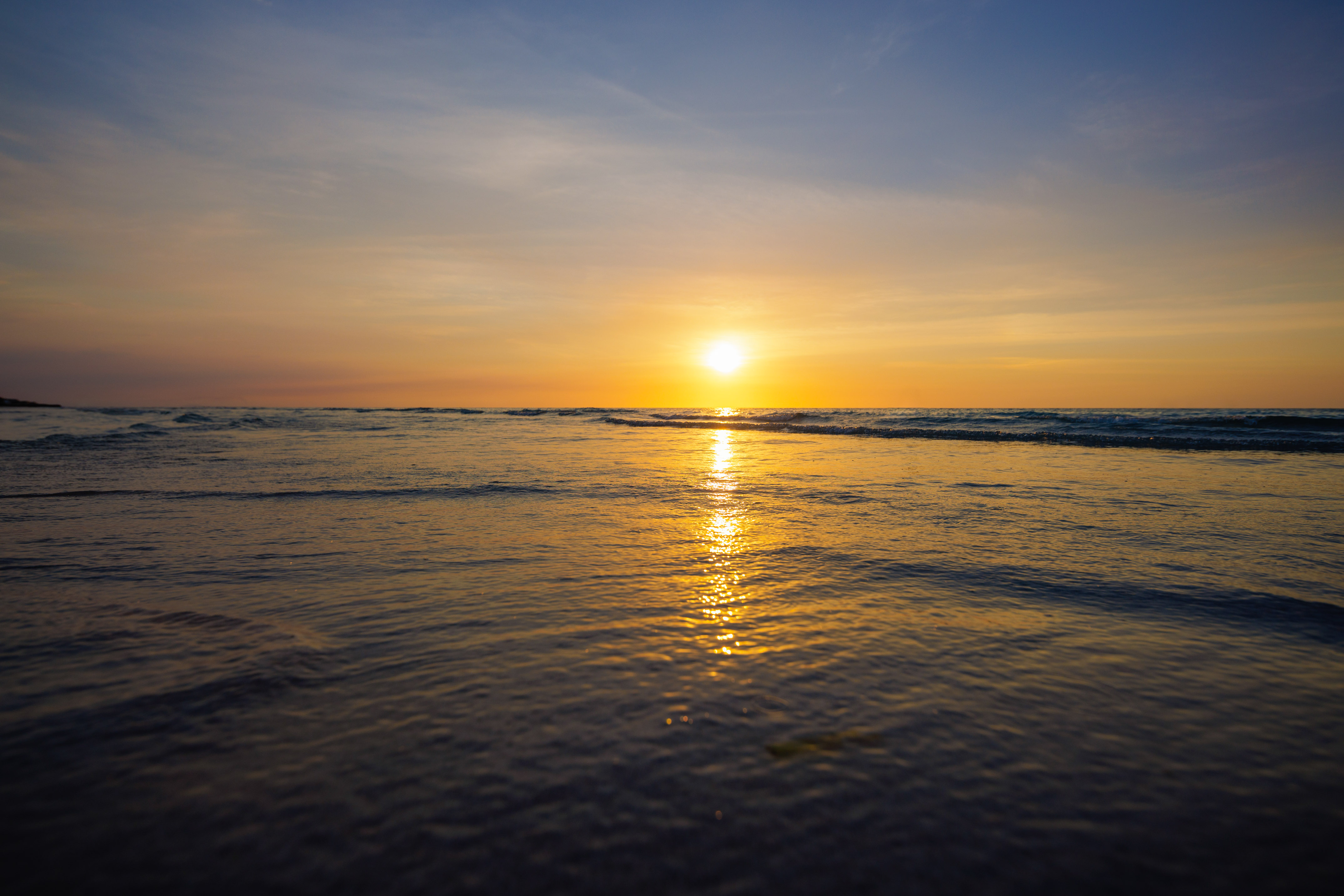 Atardecer sobre el mar, sol anaranjado en el horizonte, reflejo dorado en el agua.