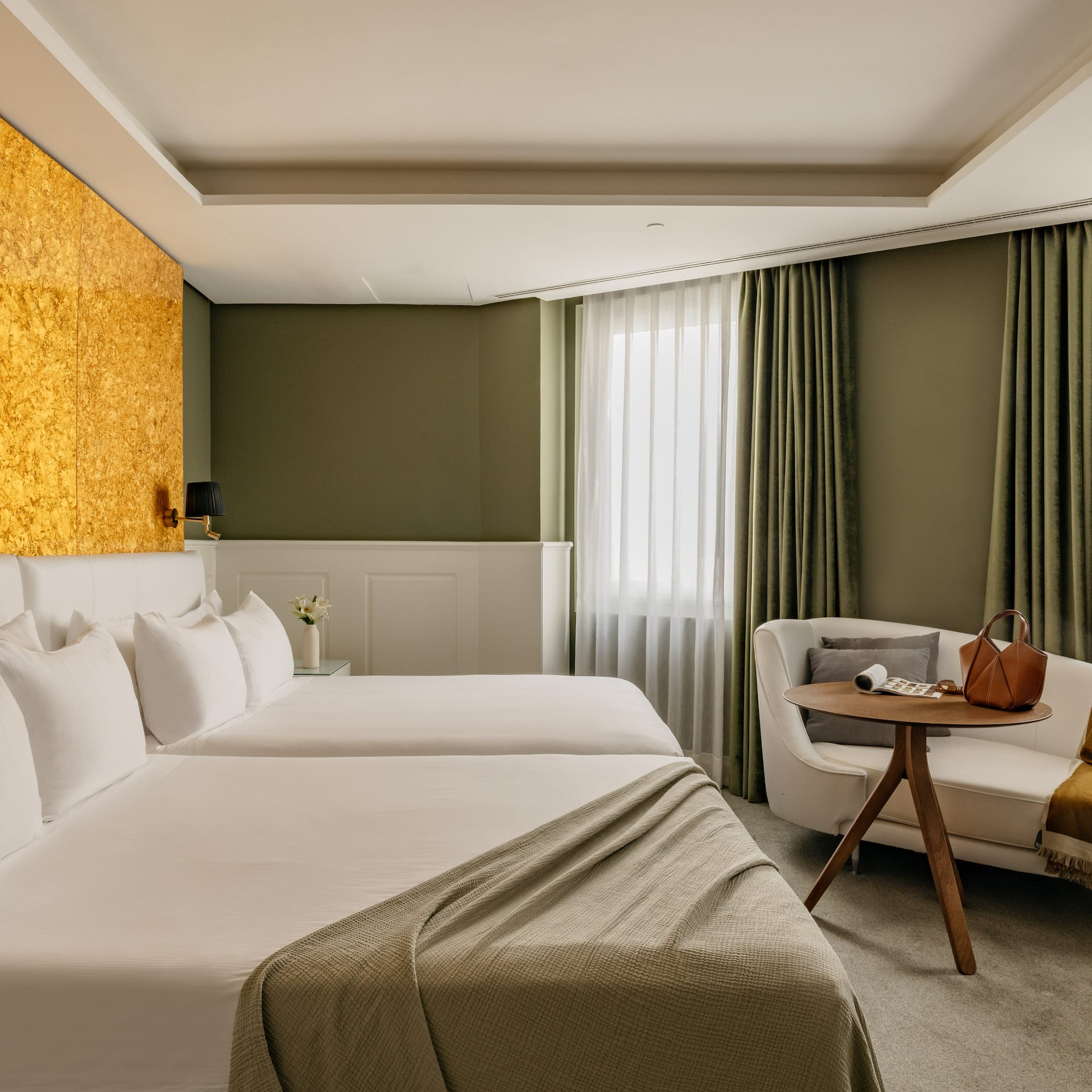 Habitación de hotel moderna con camas individuales, cabecero dorado y sofá.