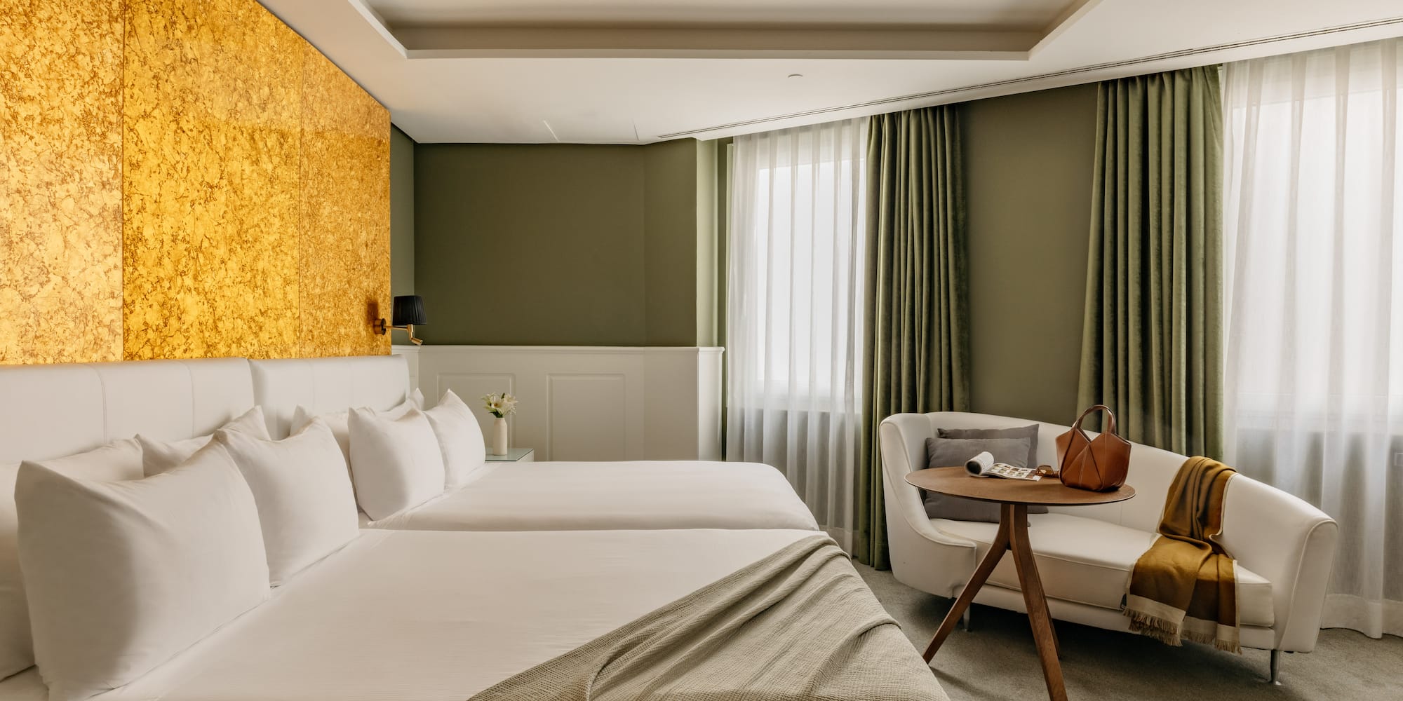 Habitación de hotel moderna con camas individuales, cabecero dorado y sofá.