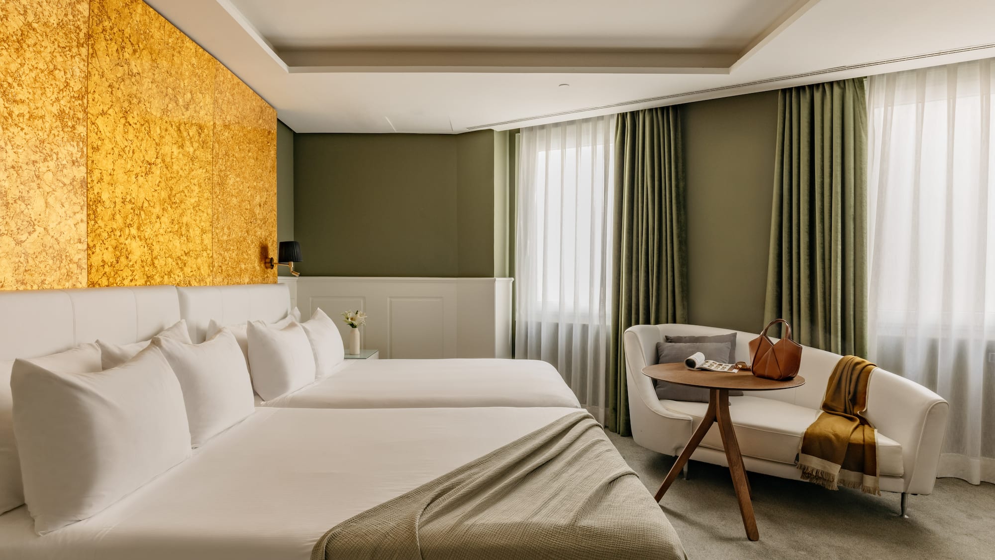 Habitación de hotel moderna con camas individuales, cabecero dorado y sofá.
