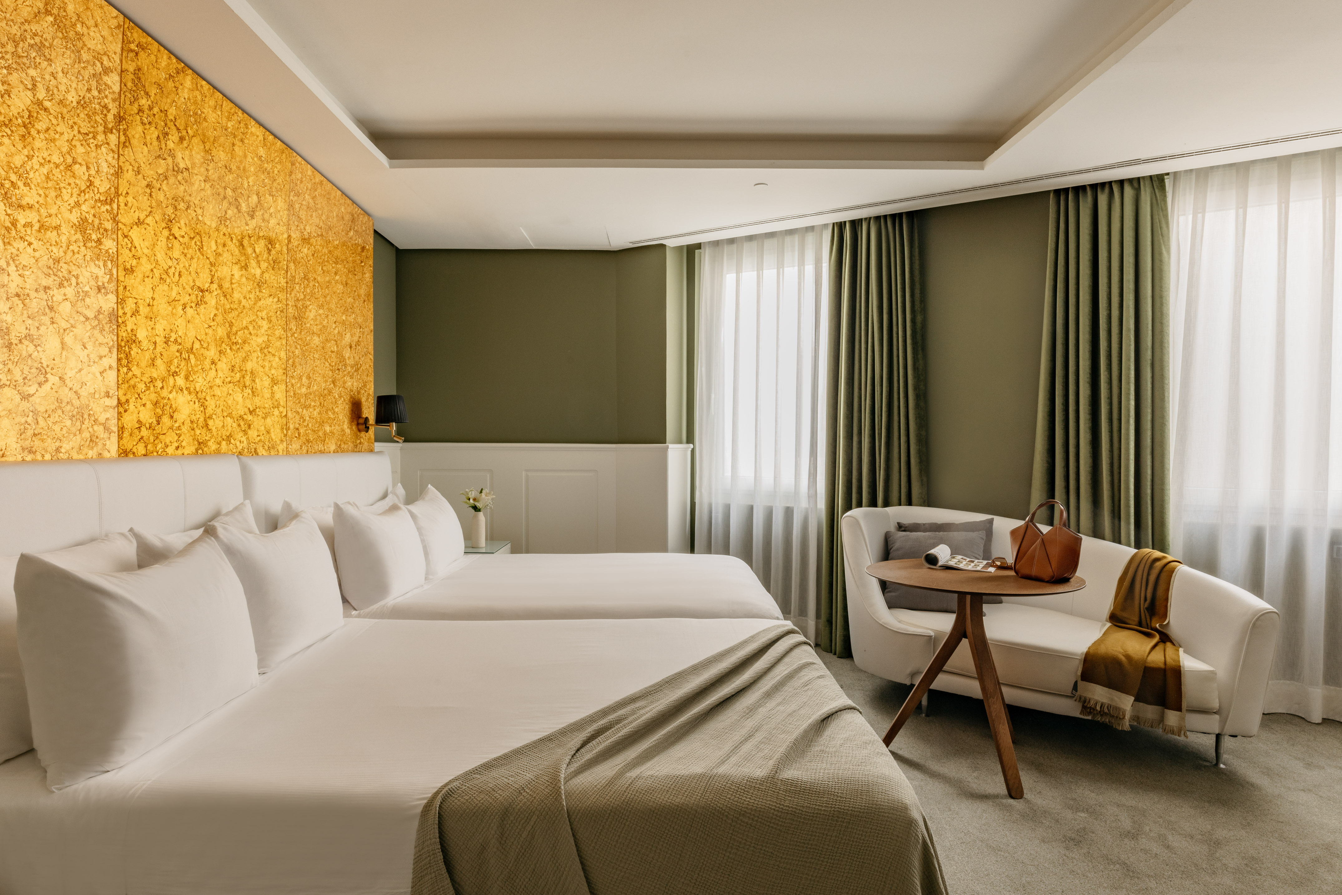 Habitación de hotel moderna con camas individuales, cabecero dorado y sofá.
