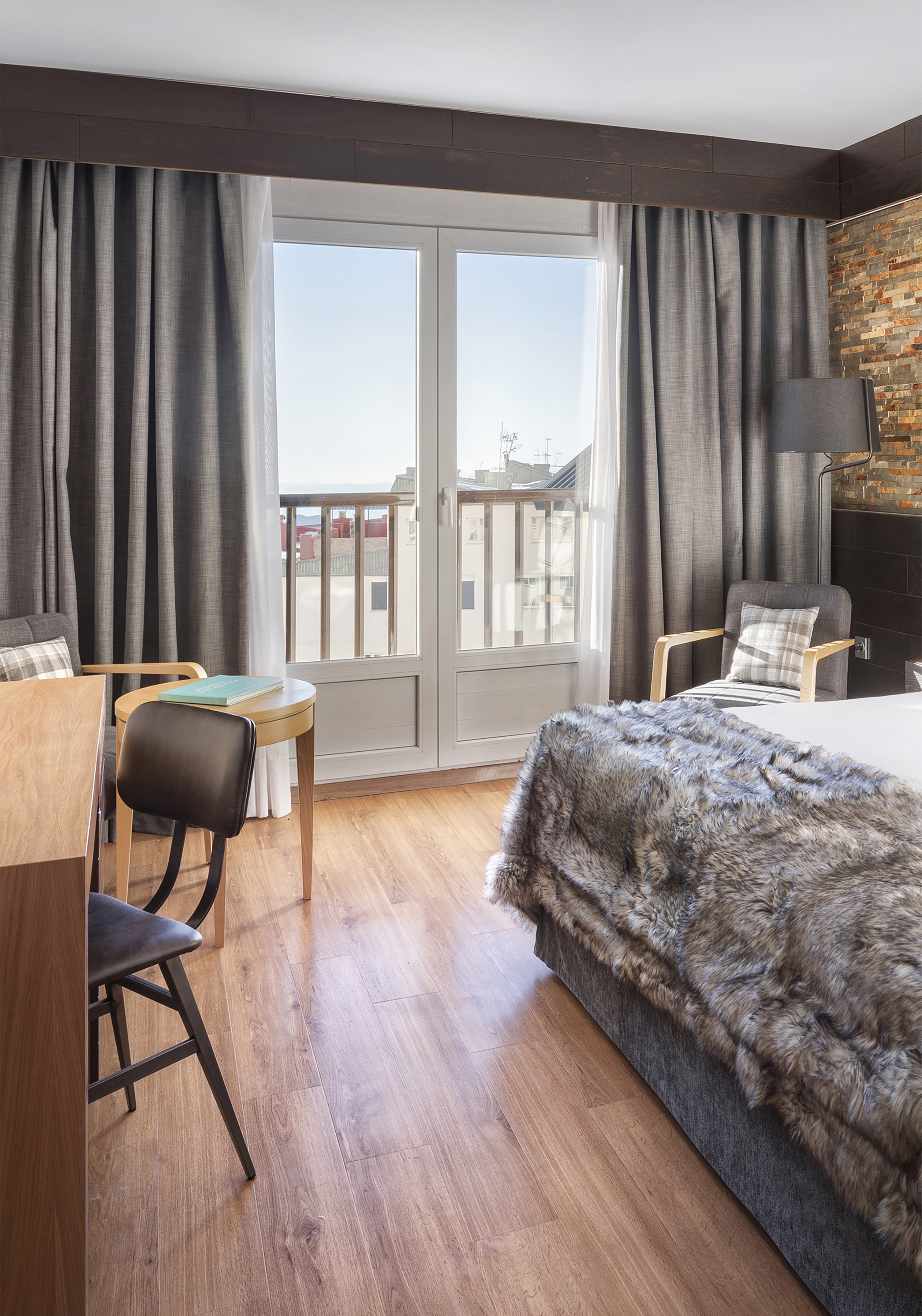 Cozy hotel bedroom with faux fur bed, balcony, wood floors, and brick wall.