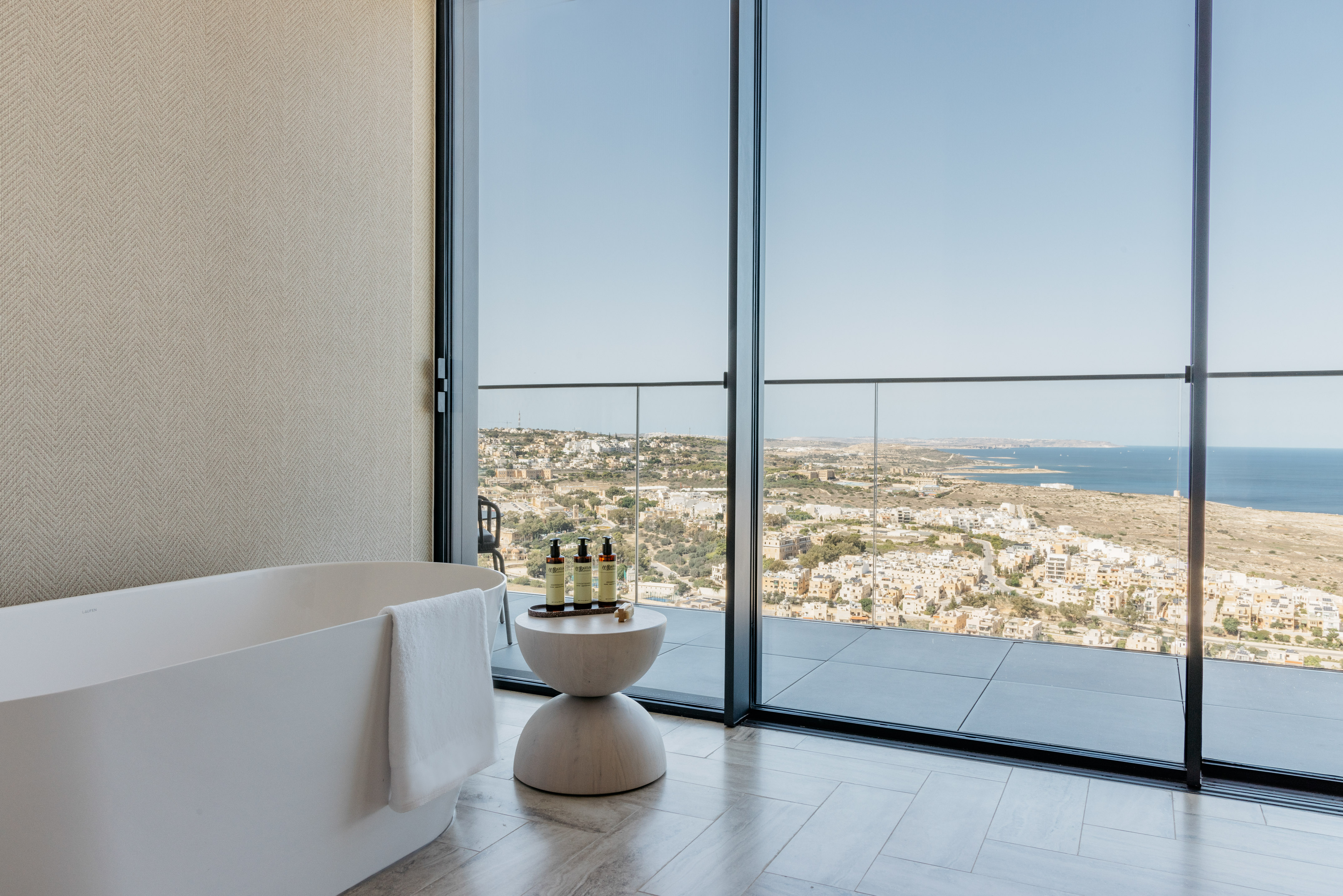 Modern luxury bathroom with freestanding tub, coastal city and sea view.