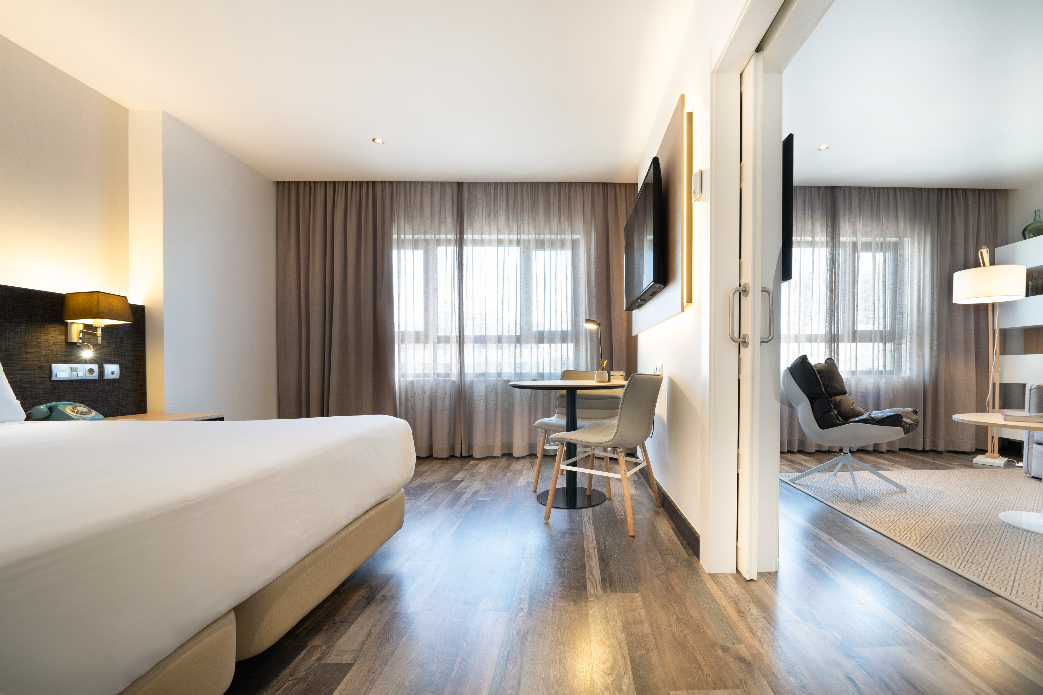 Modern hotel suite with bed, dining area, and separate lounge room.