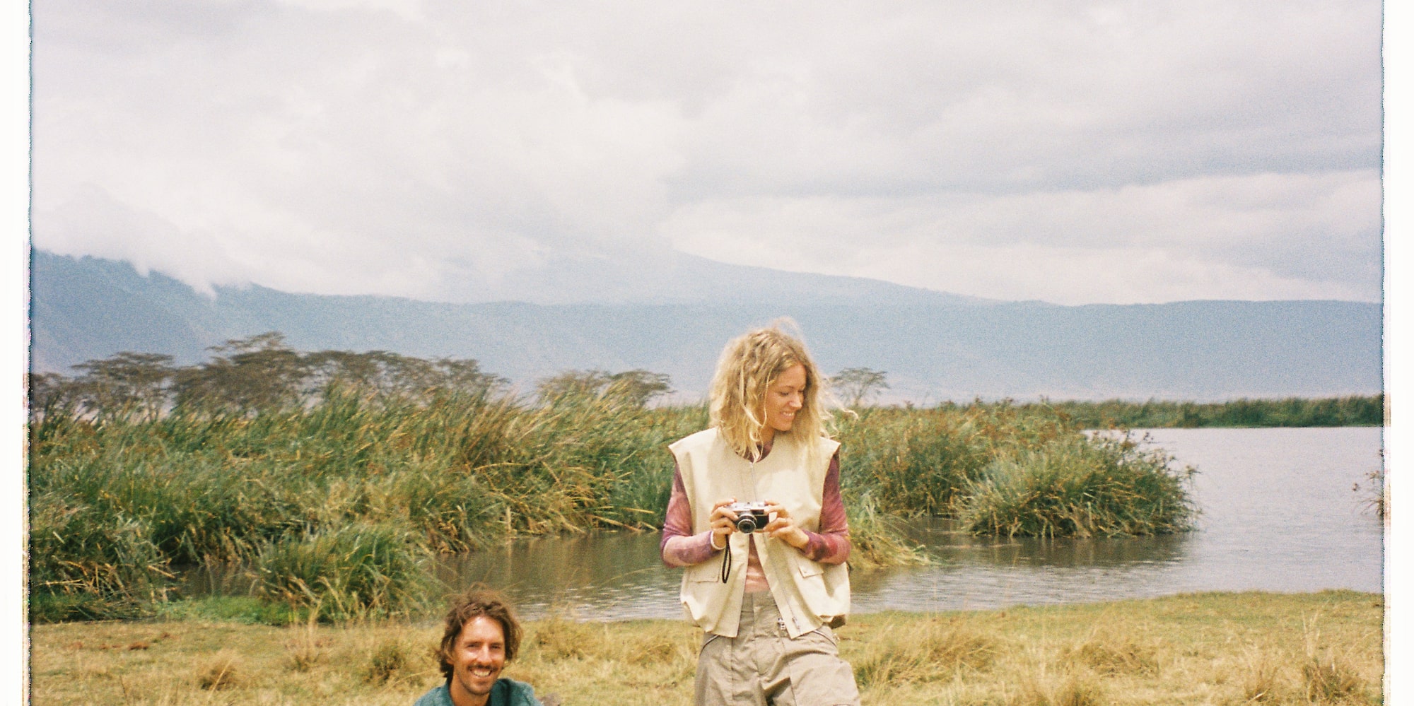 a man and woman sitting on a stump near water