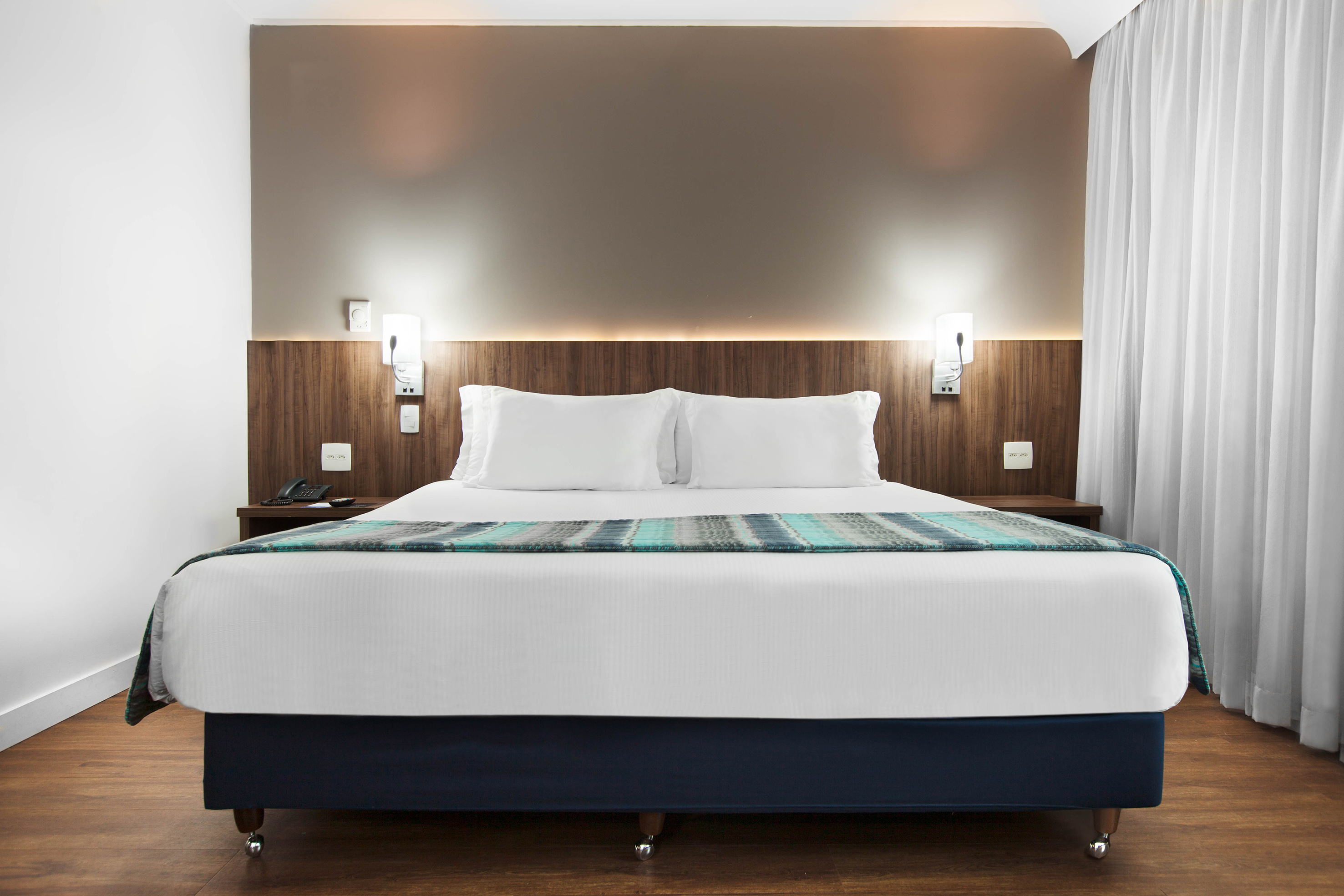 Modern hotel bedroom with queen bed, wood headboard, and warm lighting.