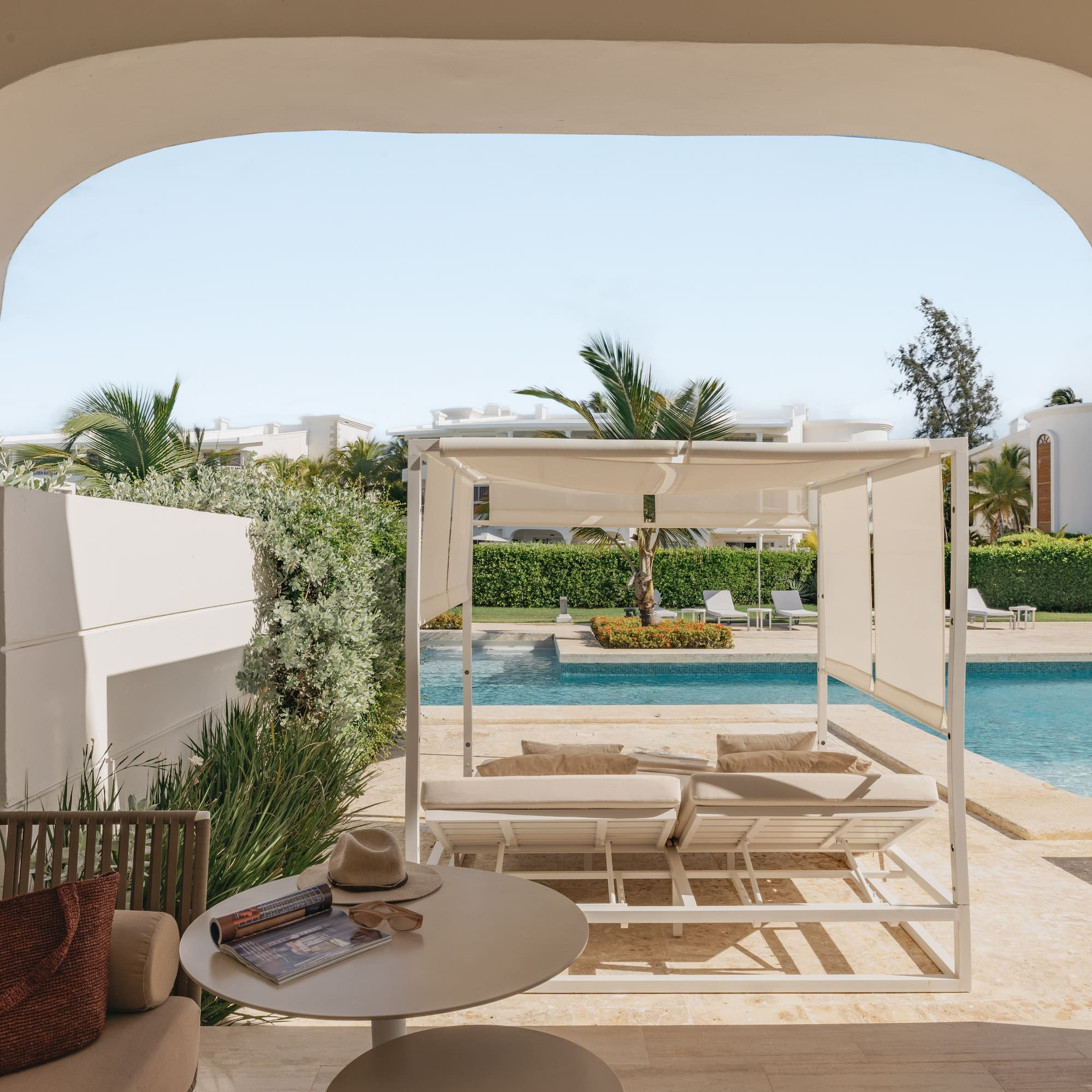 Luxury resort patio with archway, pool, white cabana, and tropical palms.