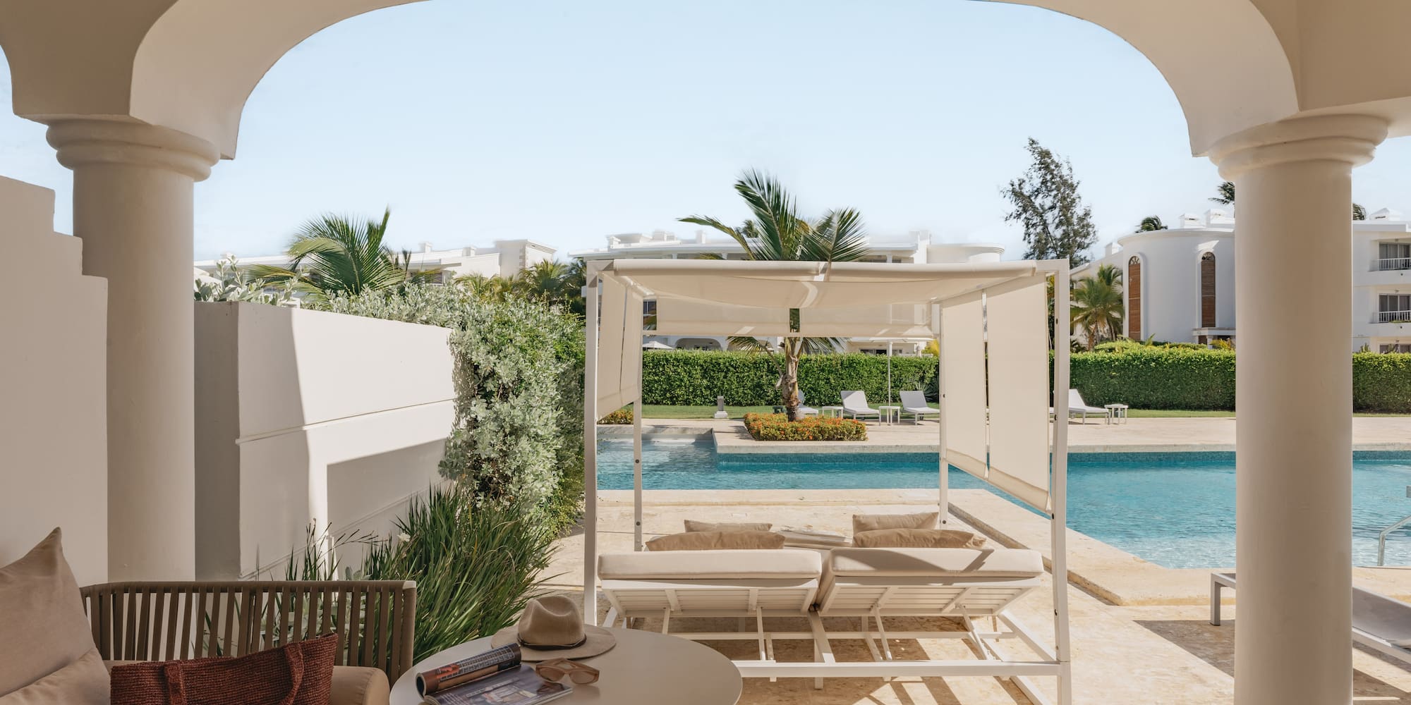 Luxury resort patio with swimming pool, white cabana, and tropical palms.