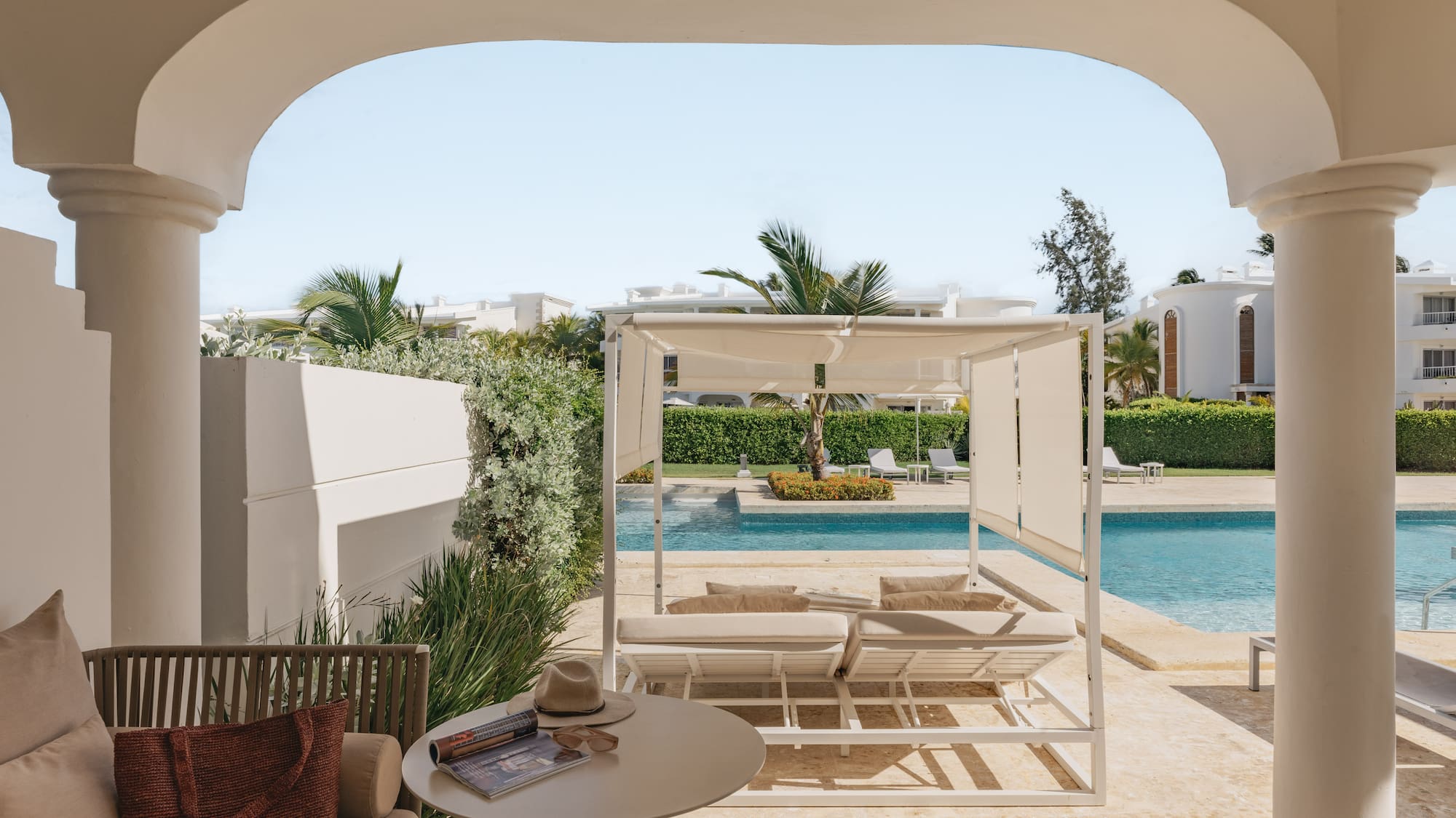 Luxury resort patio with archway, pool, white cabana, and tropical palms.