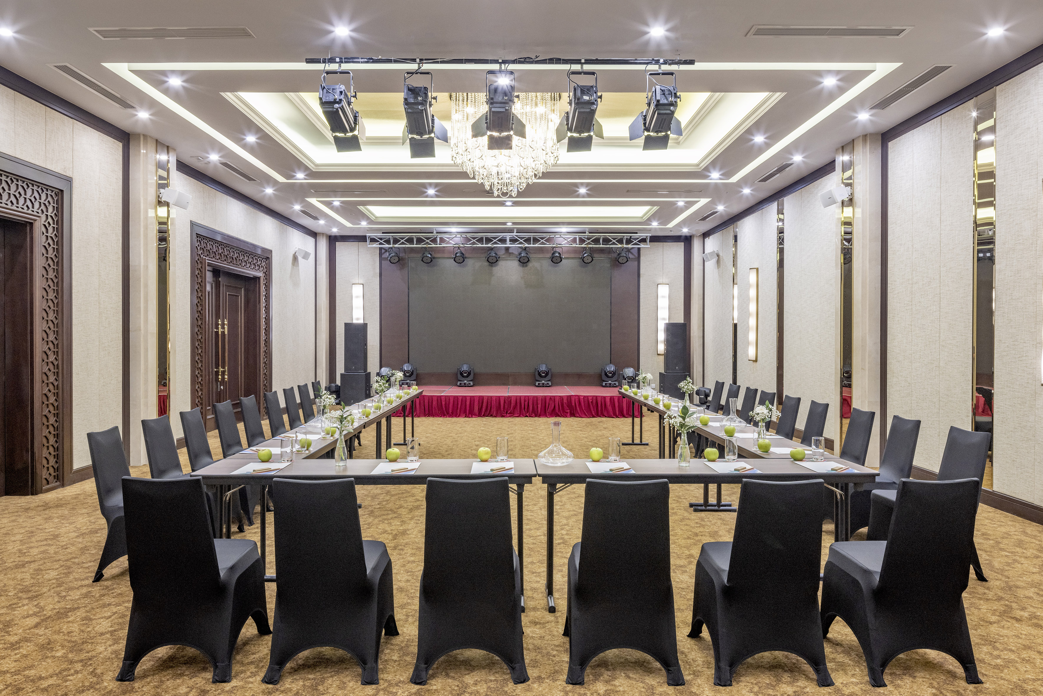 Modern U-shaped conference room with large screen, stage lights, and black chairs.