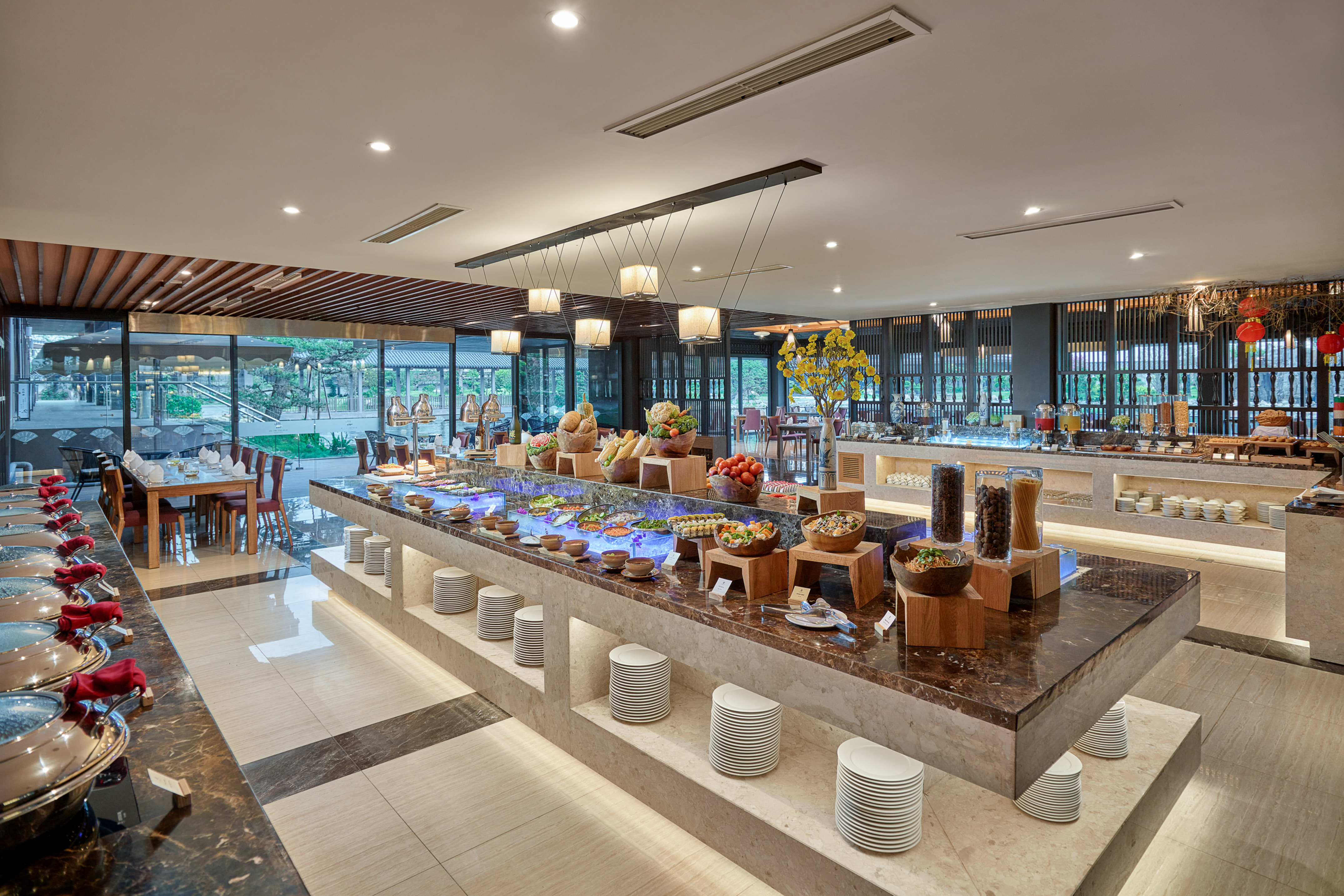 Hotel buffet restaurant with extensive food spread, modern decor, and garden view.