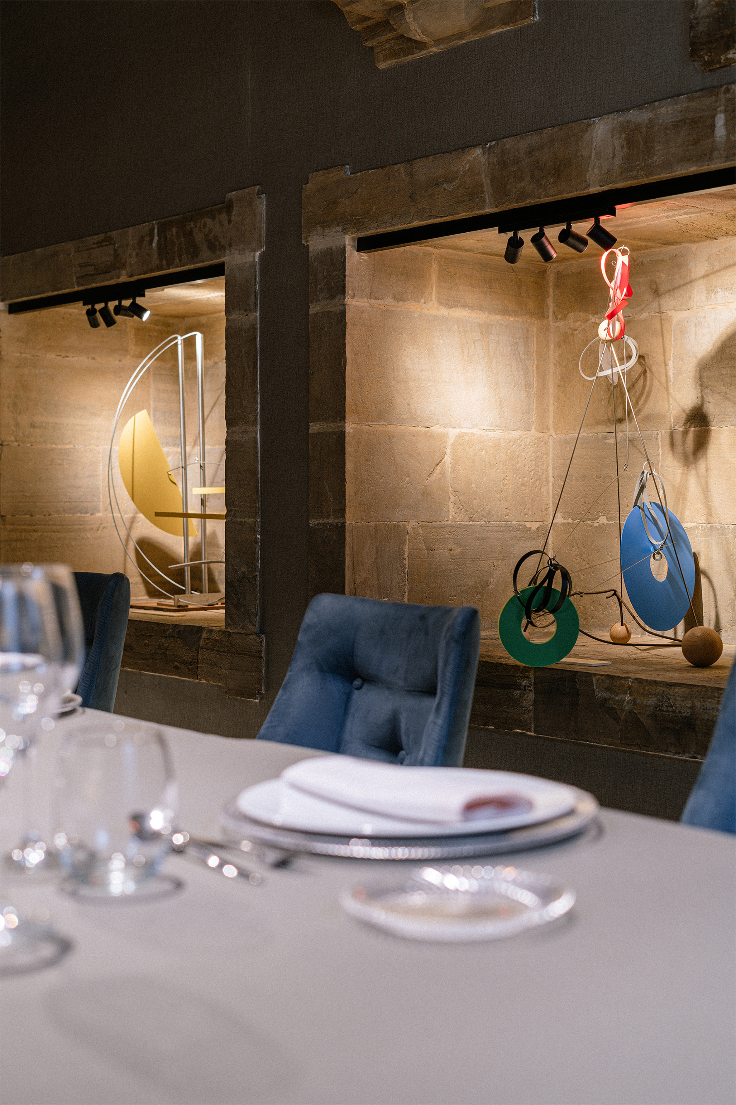 Dining table, blue chairs, modern sculptures in illuminated stone wall niches. - Archivo - Palacio de Avilés Afiliat Meliá, Avilés
