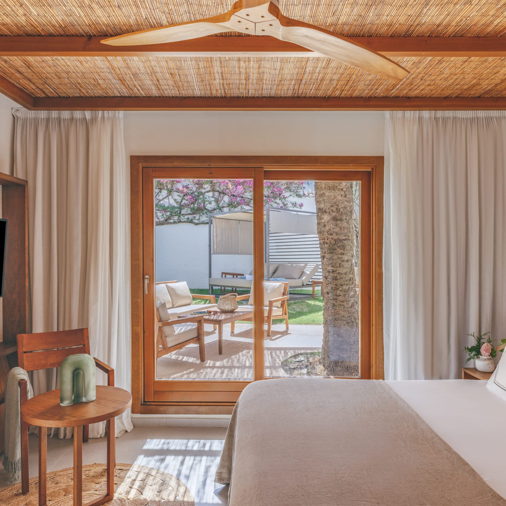 Resort bedroom with bamboo ceiling, wooden fan, and private patio garden.