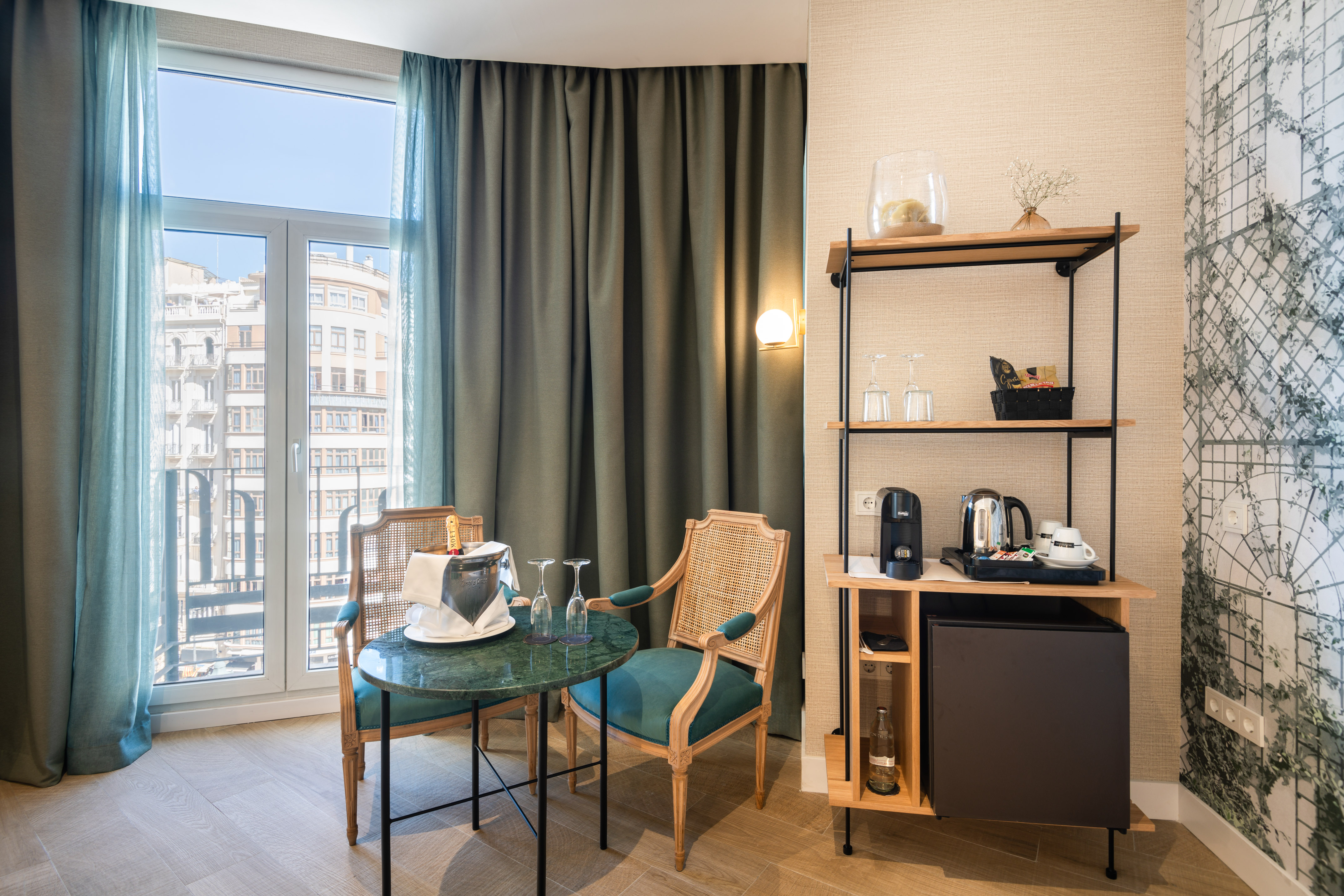 Hotel room with balcony, city view, green marble table, champagne, and minibar.