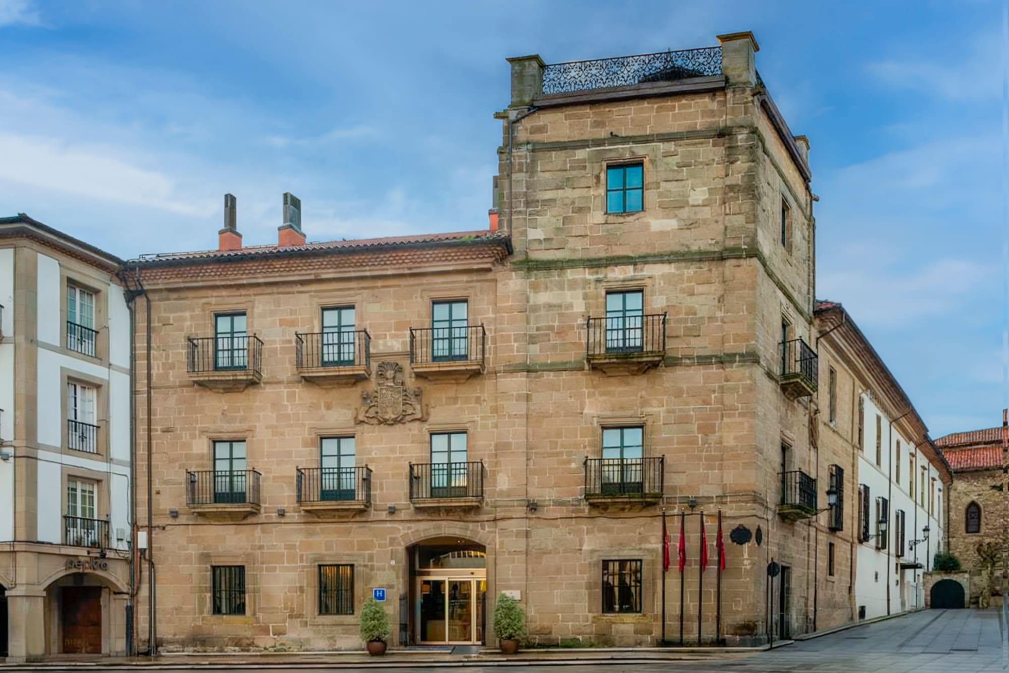Historic stone hotel building with balconies, coat of arms, and flags.