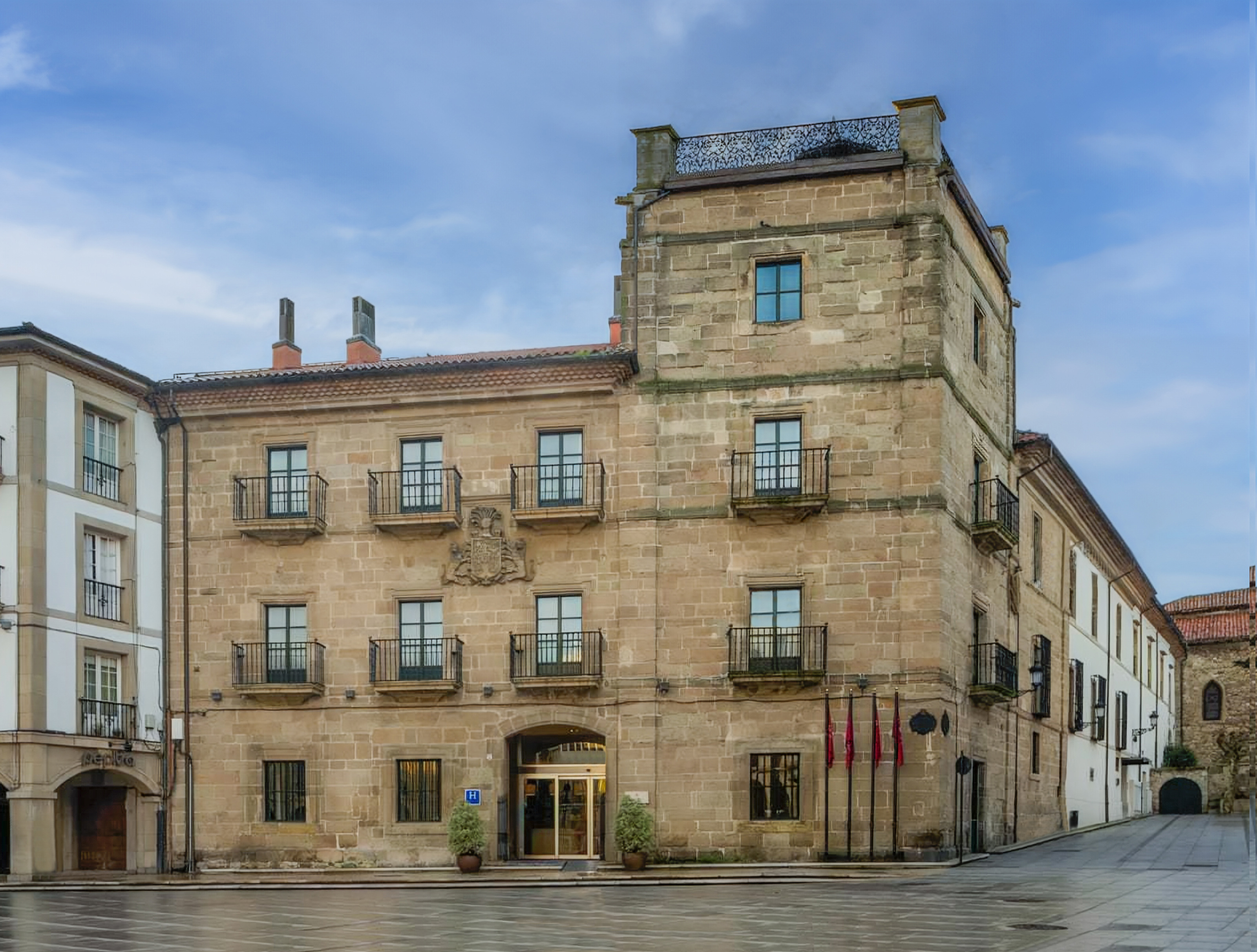 Historic stone hotel building with balconies, coat of arms, and flags.