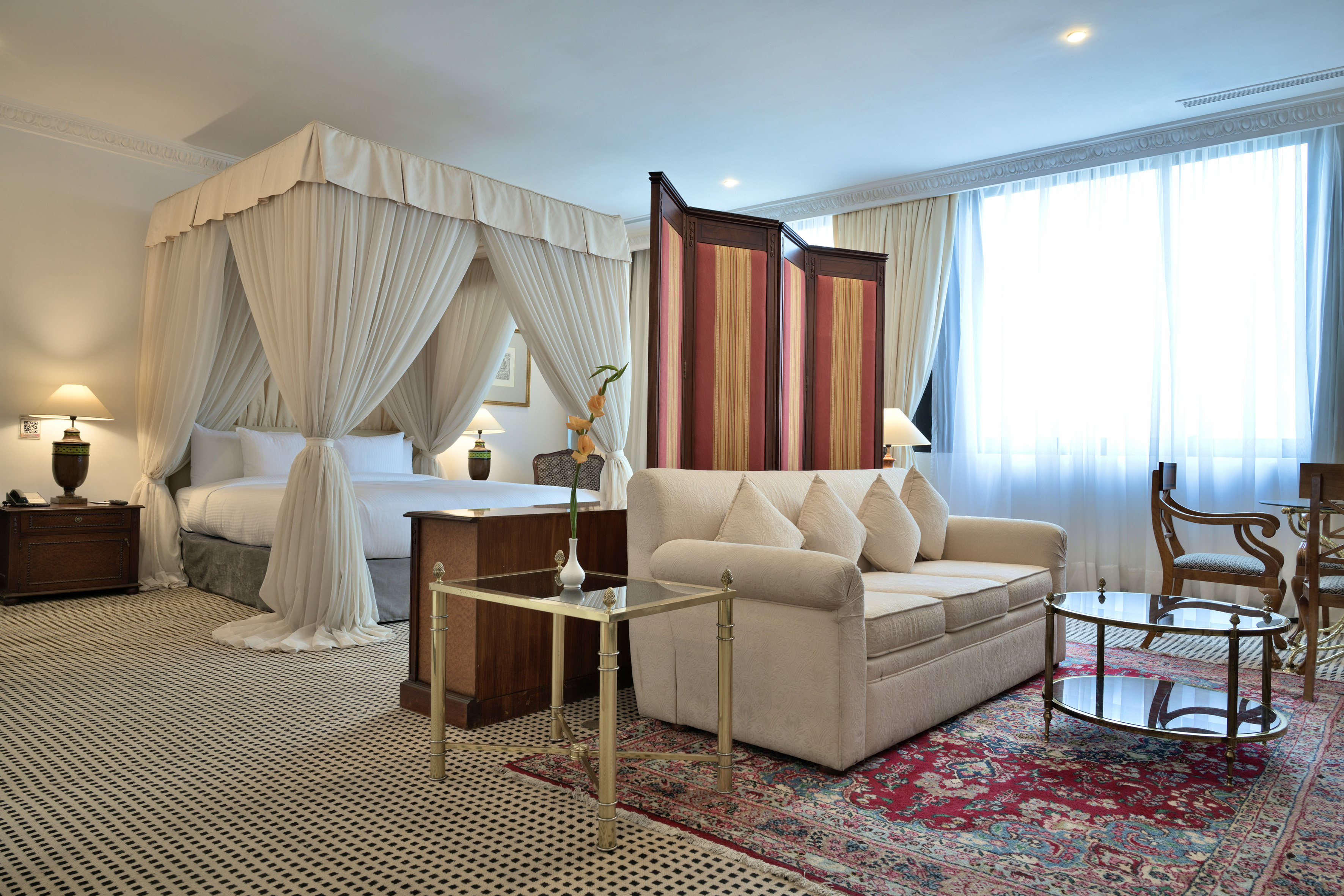Luxury hotel room with a four-poster canopy bed and sophisticated sitting area.