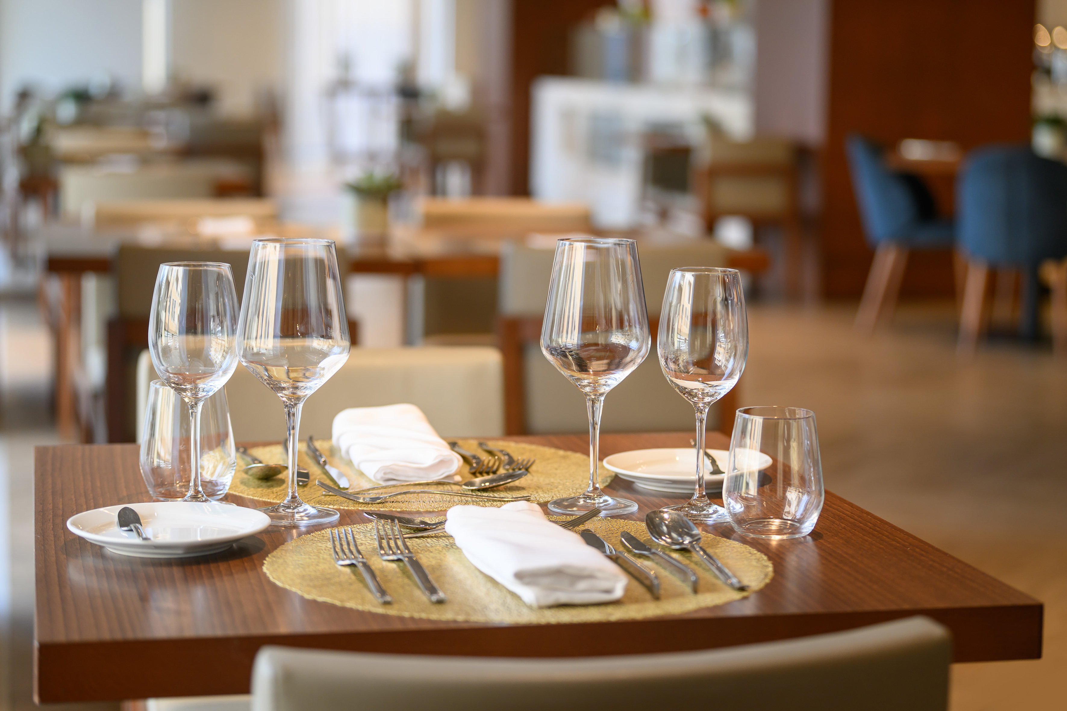 Restaurant table set with wine glasses, cutlery, white napkins, gold placemats.