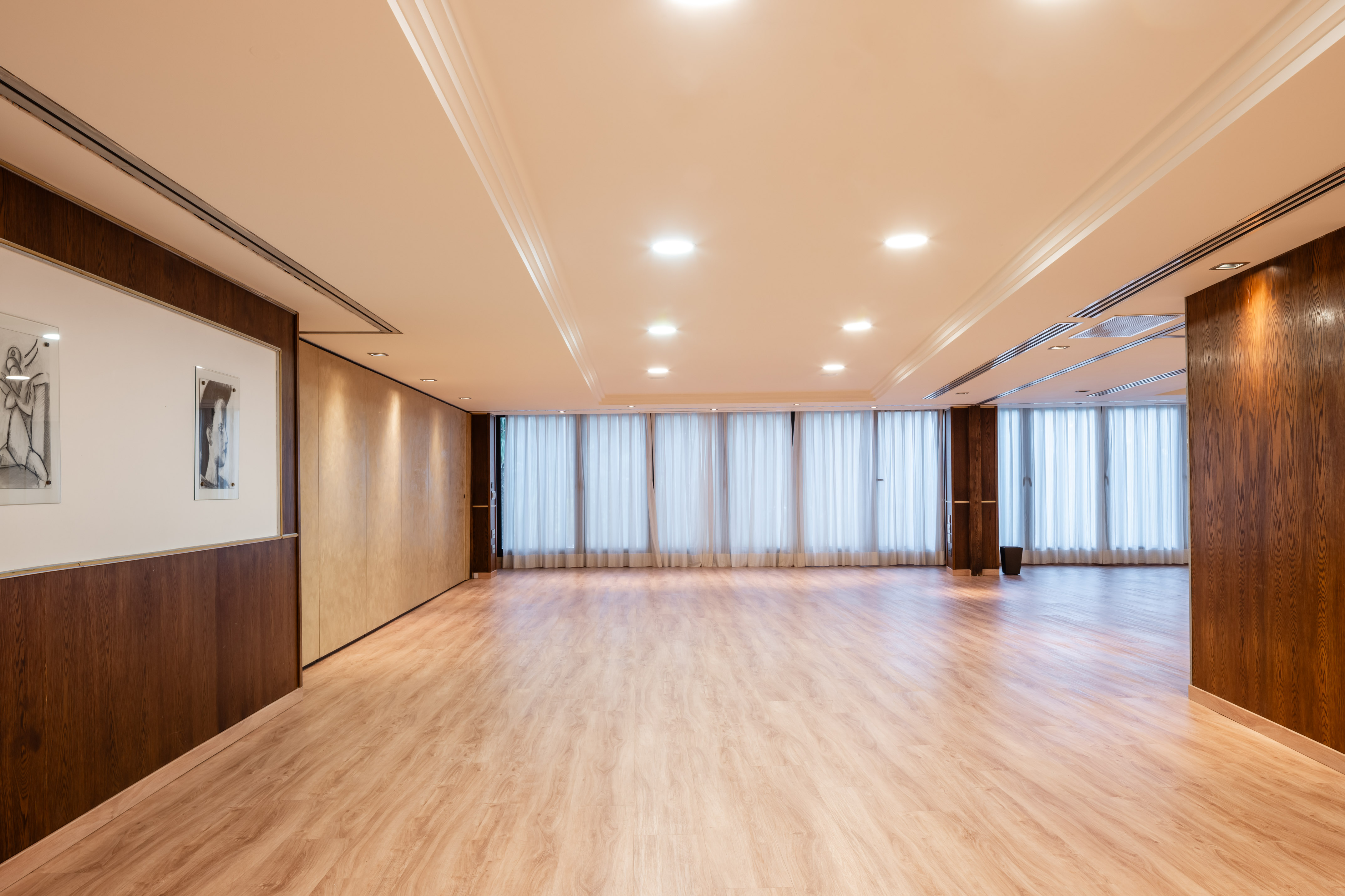 Empty modern conference room with wood floor, paneled walls, and curtains.