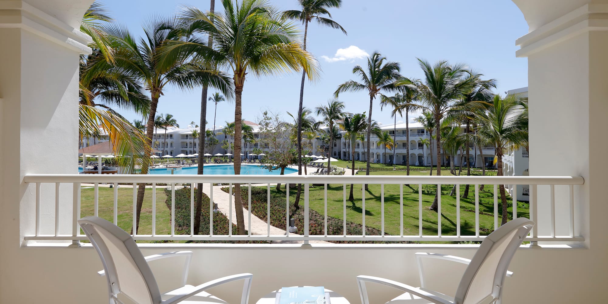 a balcony with chairs and a table and a pool in the background