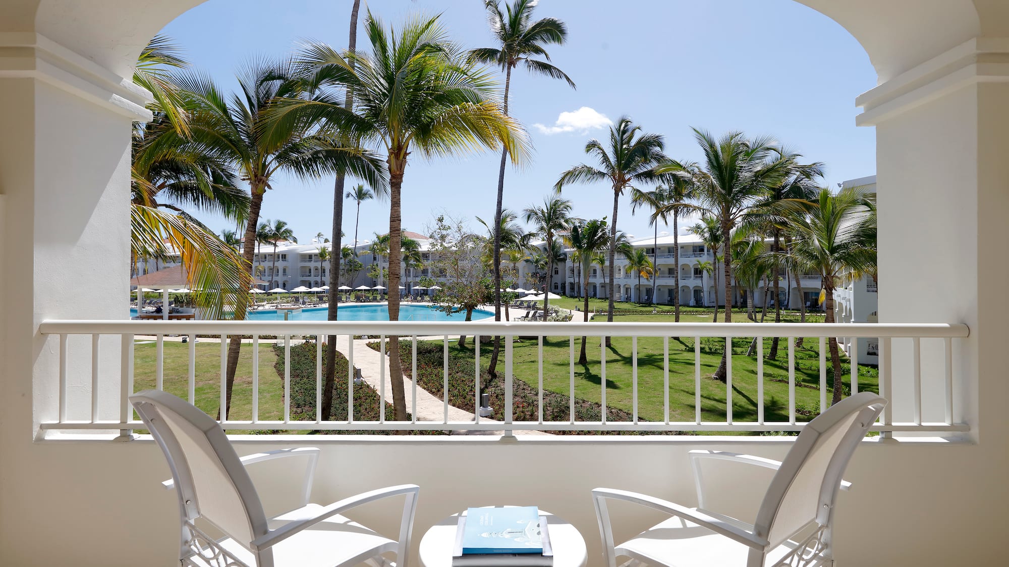 a balcony with chairs and a table and a pool in the background